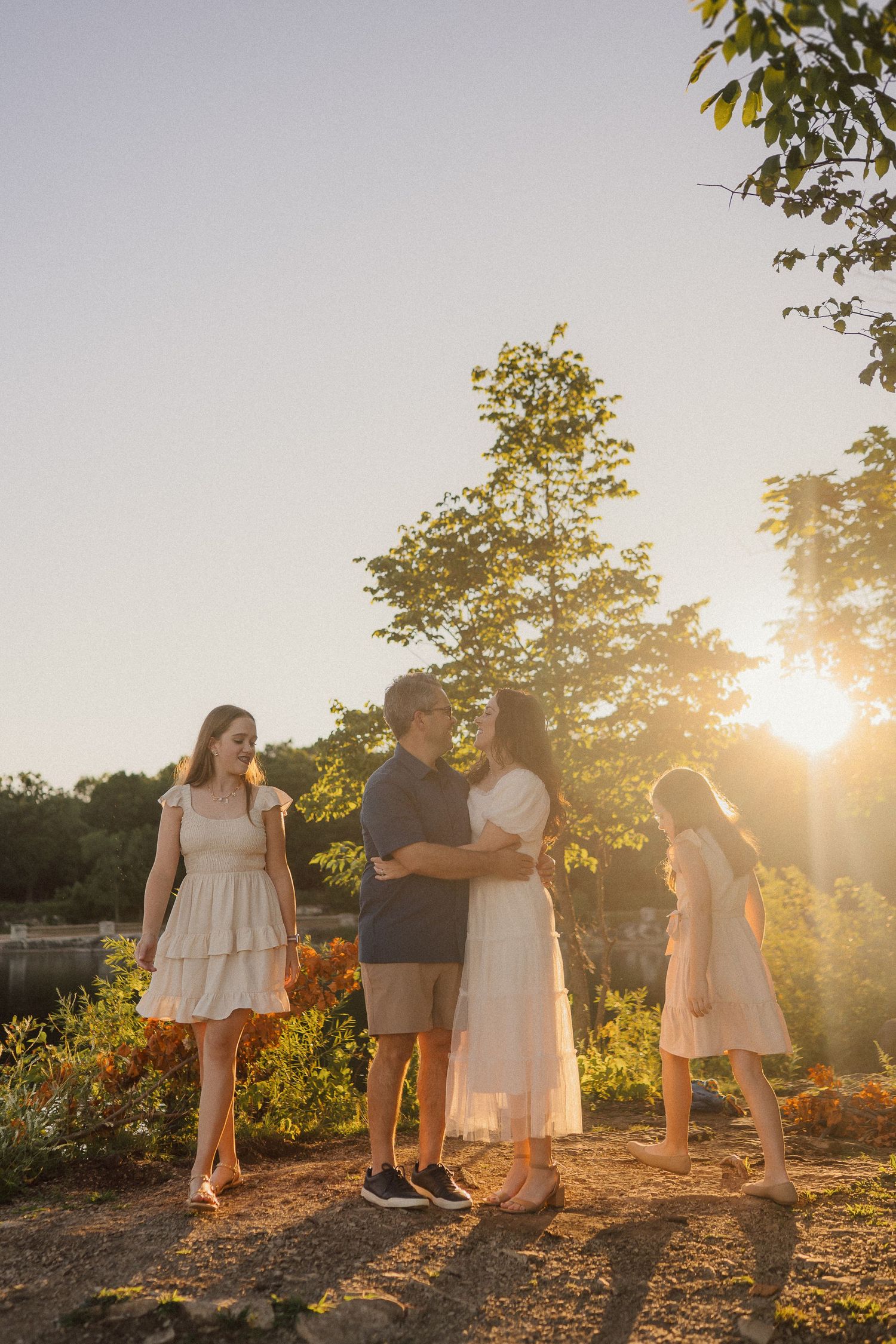 A family stands together on a hilltop during sunset with golden light filtering through trees.