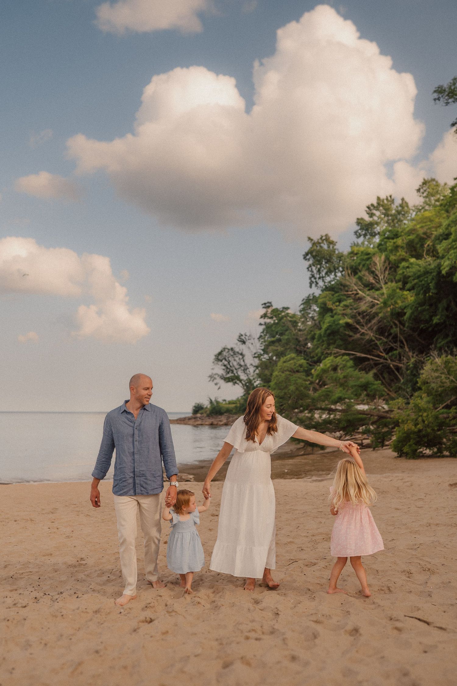 A family holding hands while strolling on a beautiful beach with fluffy clouds overhead.