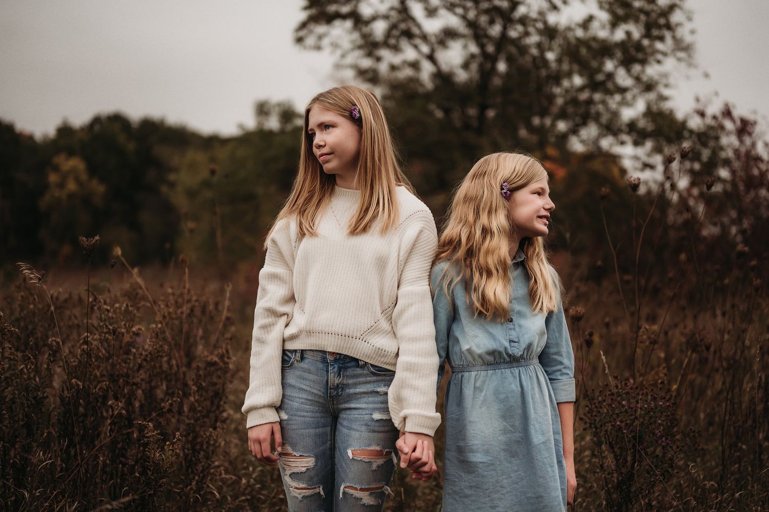 Two young people stand together in casual attire against an autumn meadow backdrop.