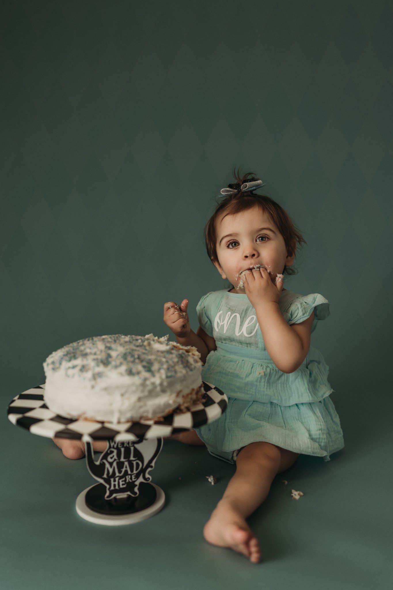 A cake smash photo session with a white frosted cake on a black and white striped cake stand.