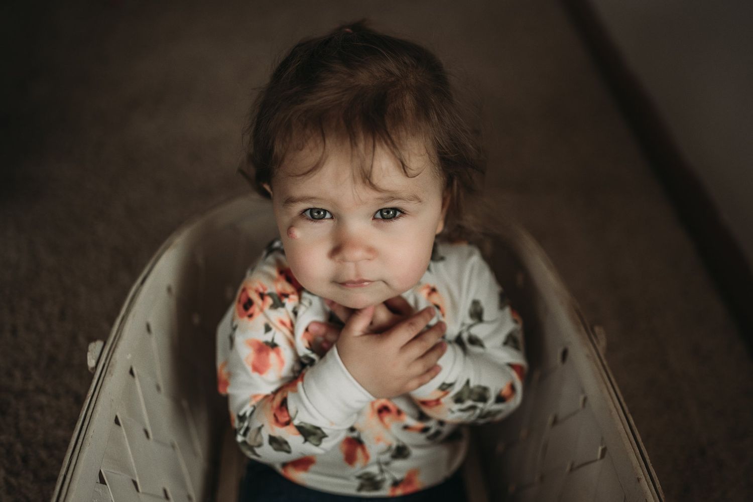 A toddler in a floral print shirt sits in a chair and smiles at the camera.