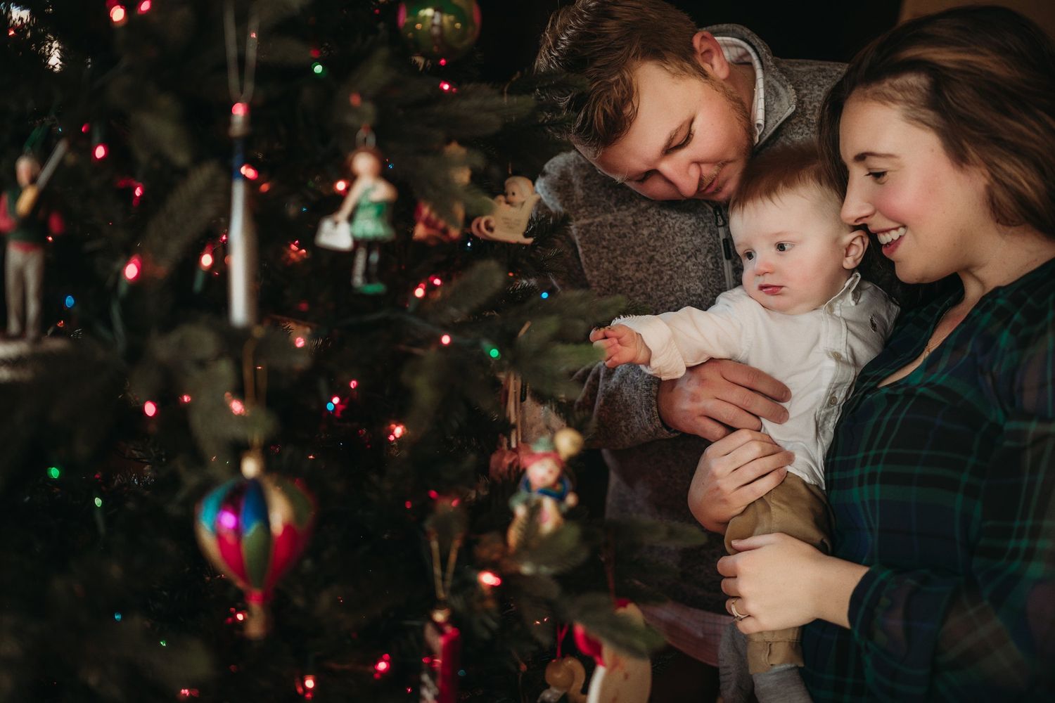 Family gathered around their Christmas tree, examining ornaments together in warm lighting.