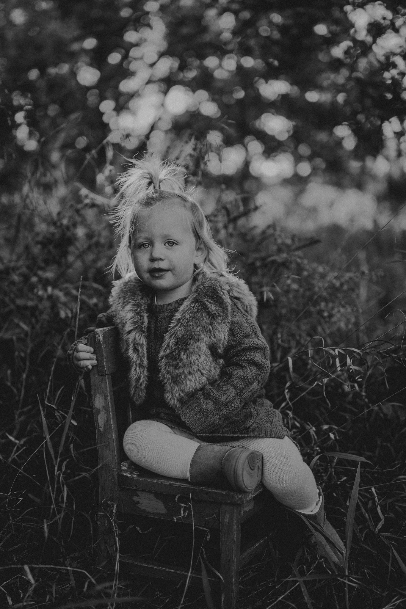 Child sitting on wooden chair in nature with bokeh background.