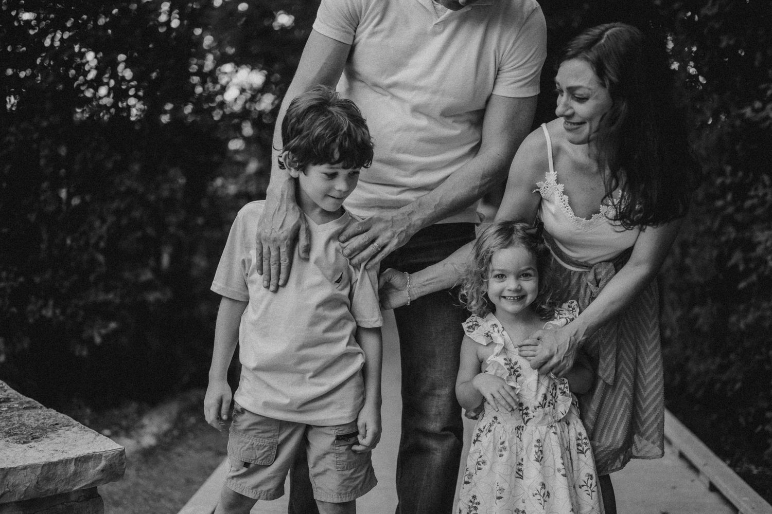 A black and white portrait of a family standing together on a wooden walkway.