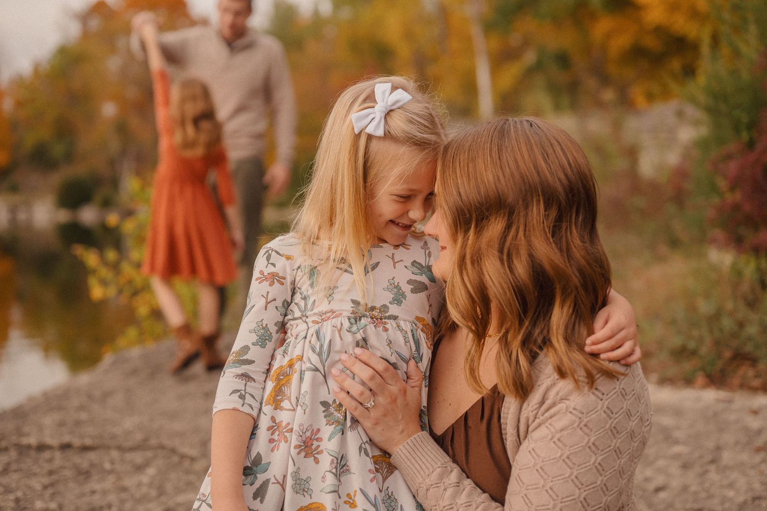 Two people share an intimate moment outdoors during autumn with fall foliage and warm lighting in the background.