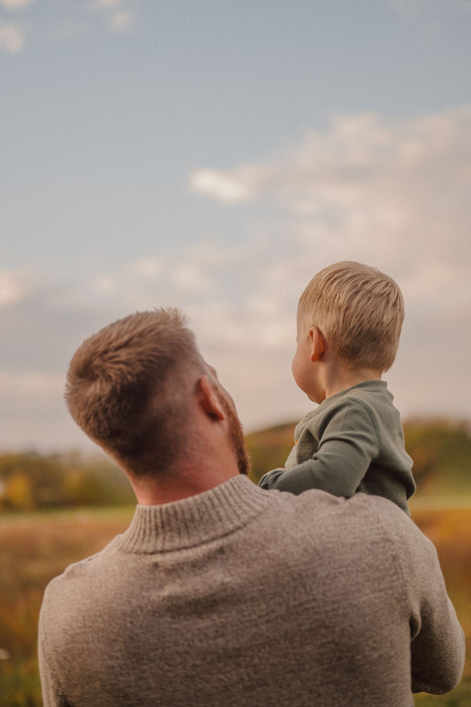 Parent and child silhouetted against soft sky during outdoor portrait session.