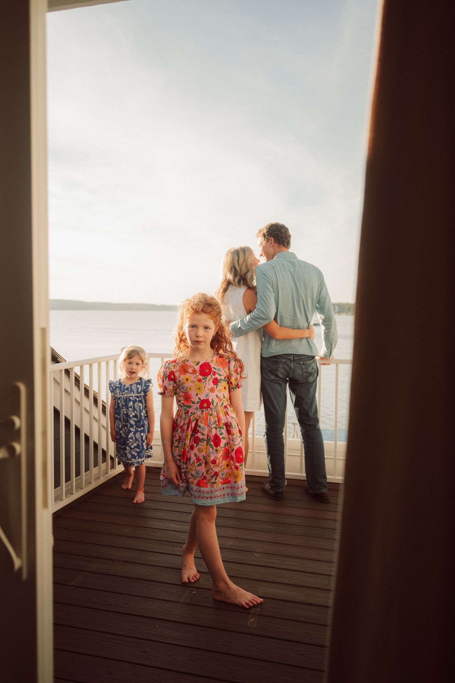 People gather on a wooden deck overlooking a scenic waterfront view during sunset.