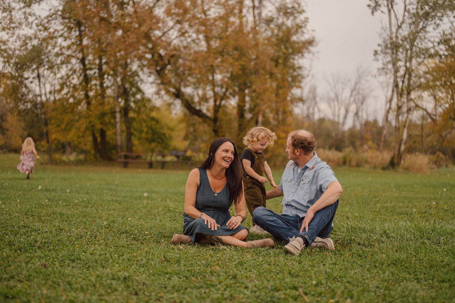 A family relaxes together in a peaceful meadow surrounded by fall colors.