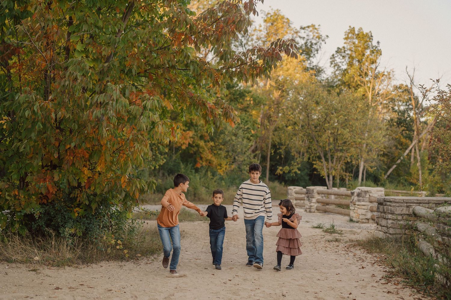 A family walks together on a stone path surrounded by autumn trees during golden hour.