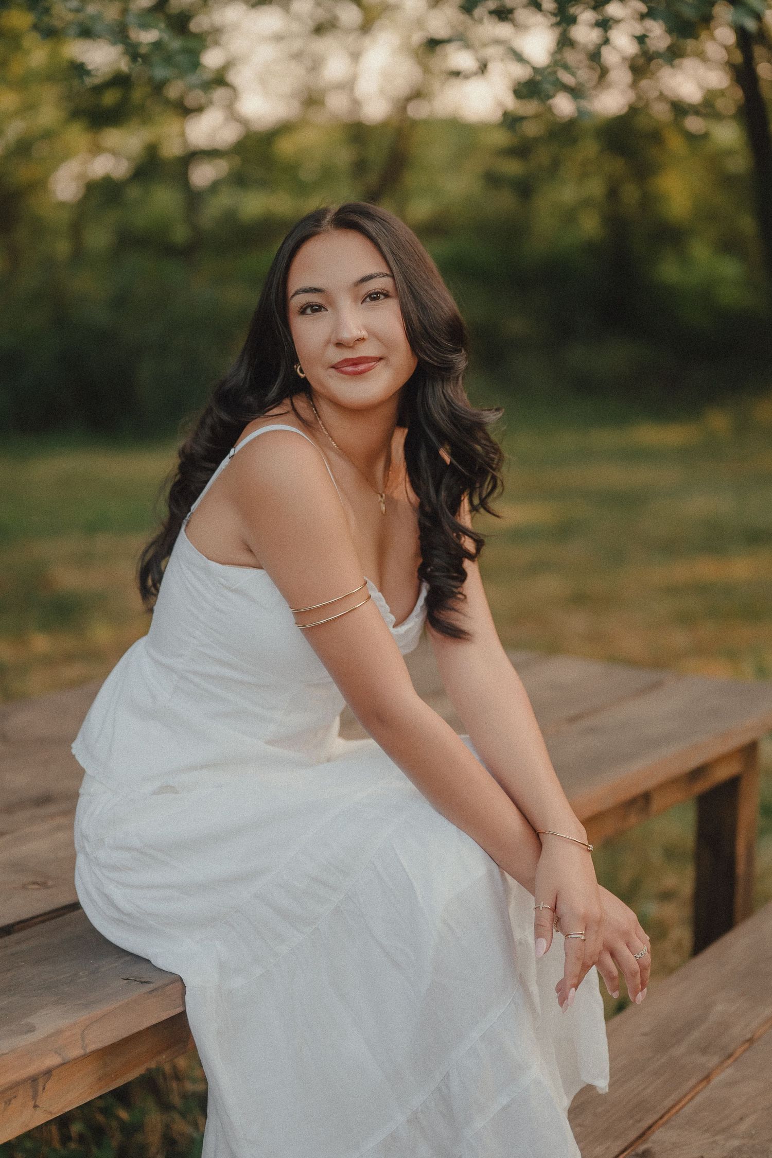 Young woman in white dress sitting on wooden steps outdoors in golden hour light.