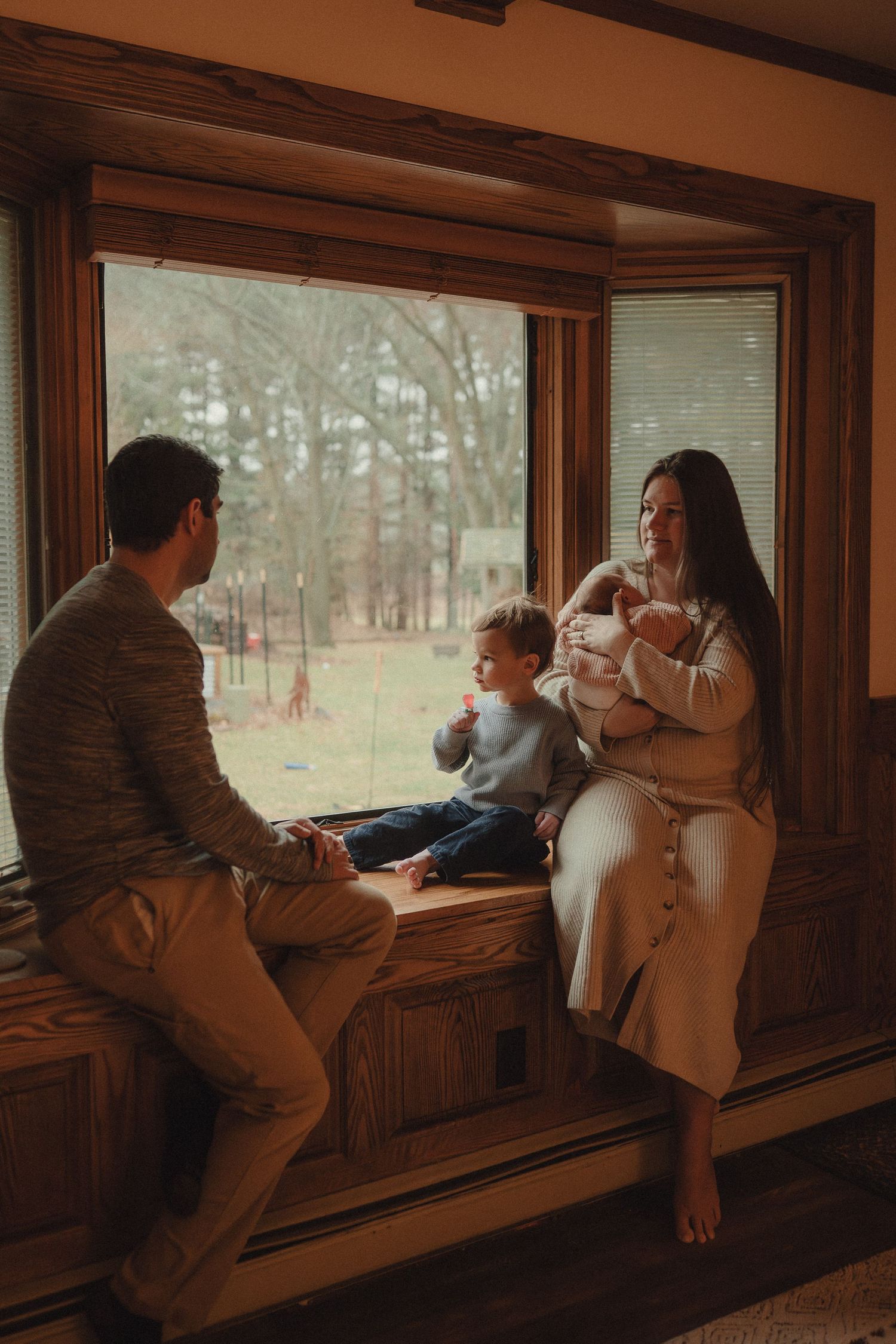 Family members sit together on a wooden window bench overlooking a scenic forest view.