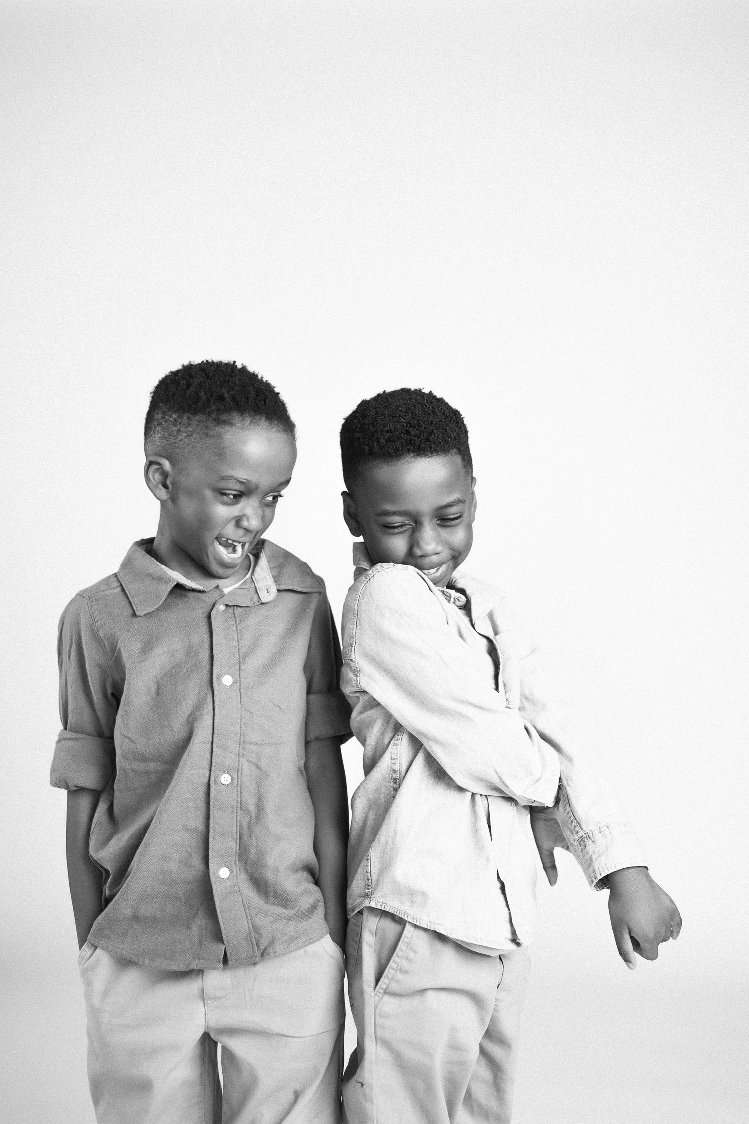 Two young children in light colored clothing laugh and play together in a studio setting.