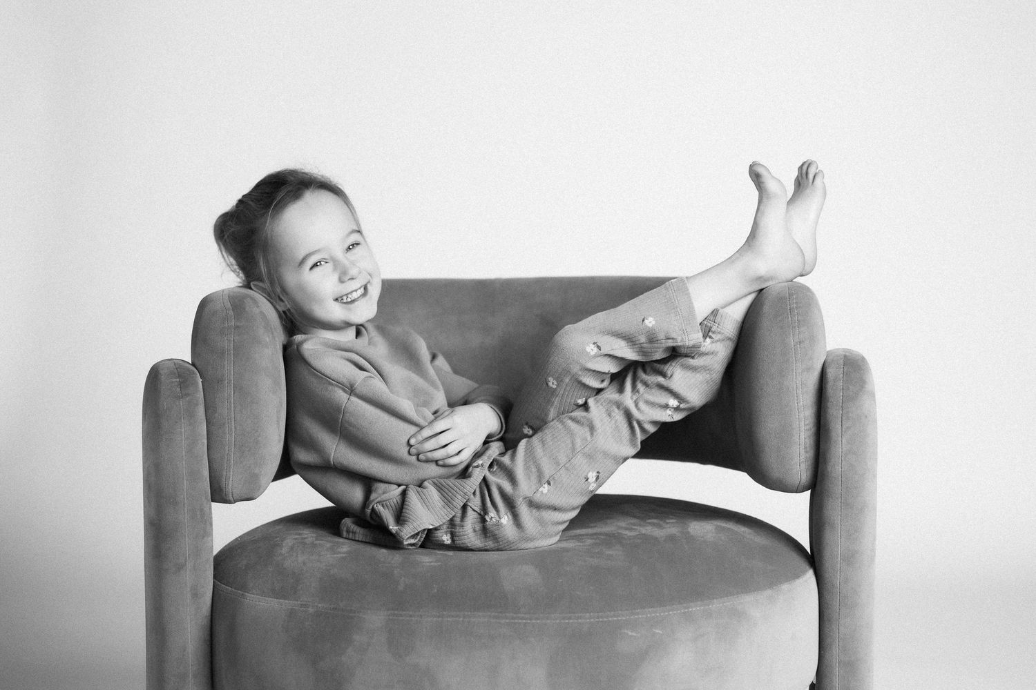 Black and white photo of a child relaxing with feet up on a comfortable armchair.