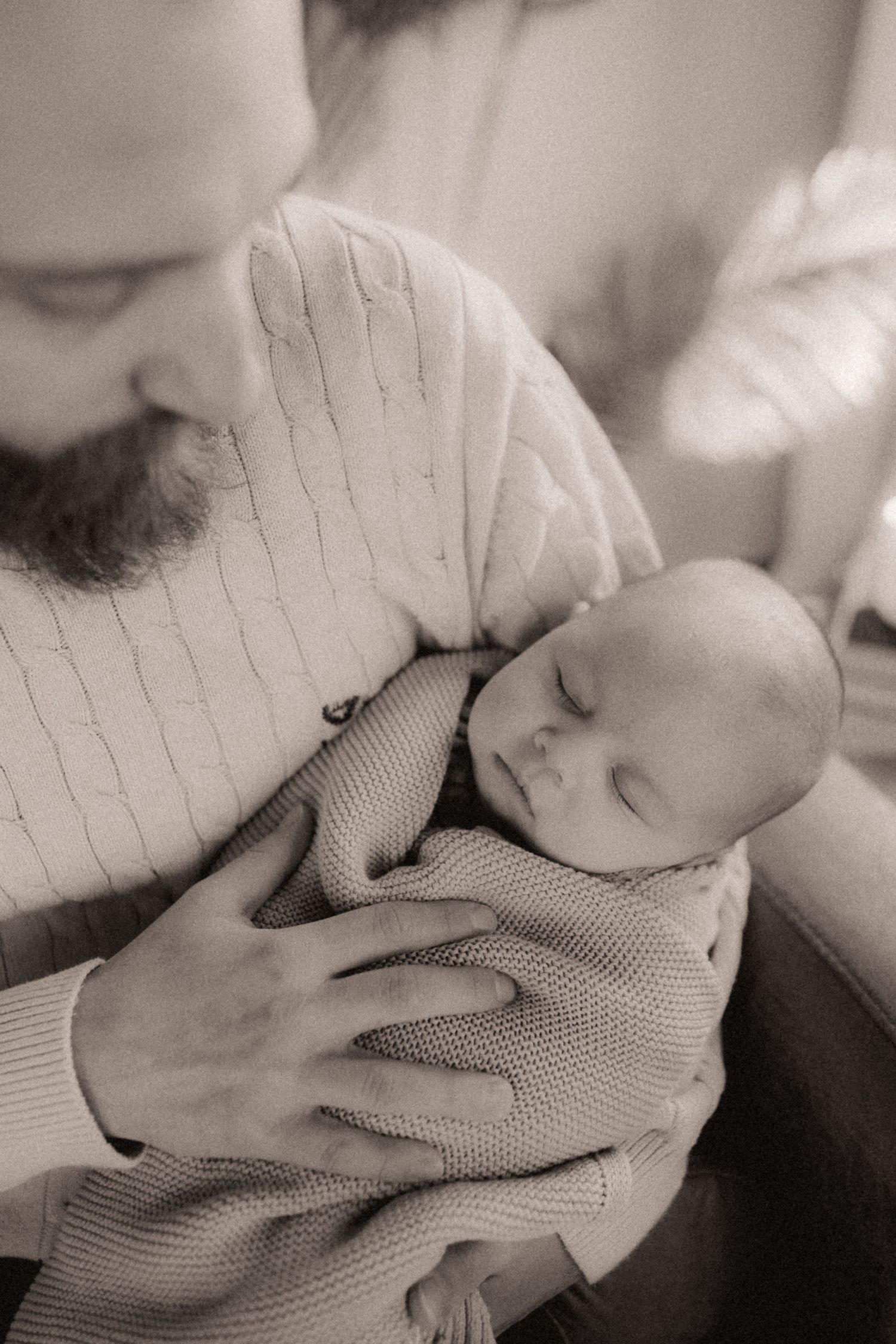 Black and white intimate portrait of sleeping baby wrapped in knit blanket.