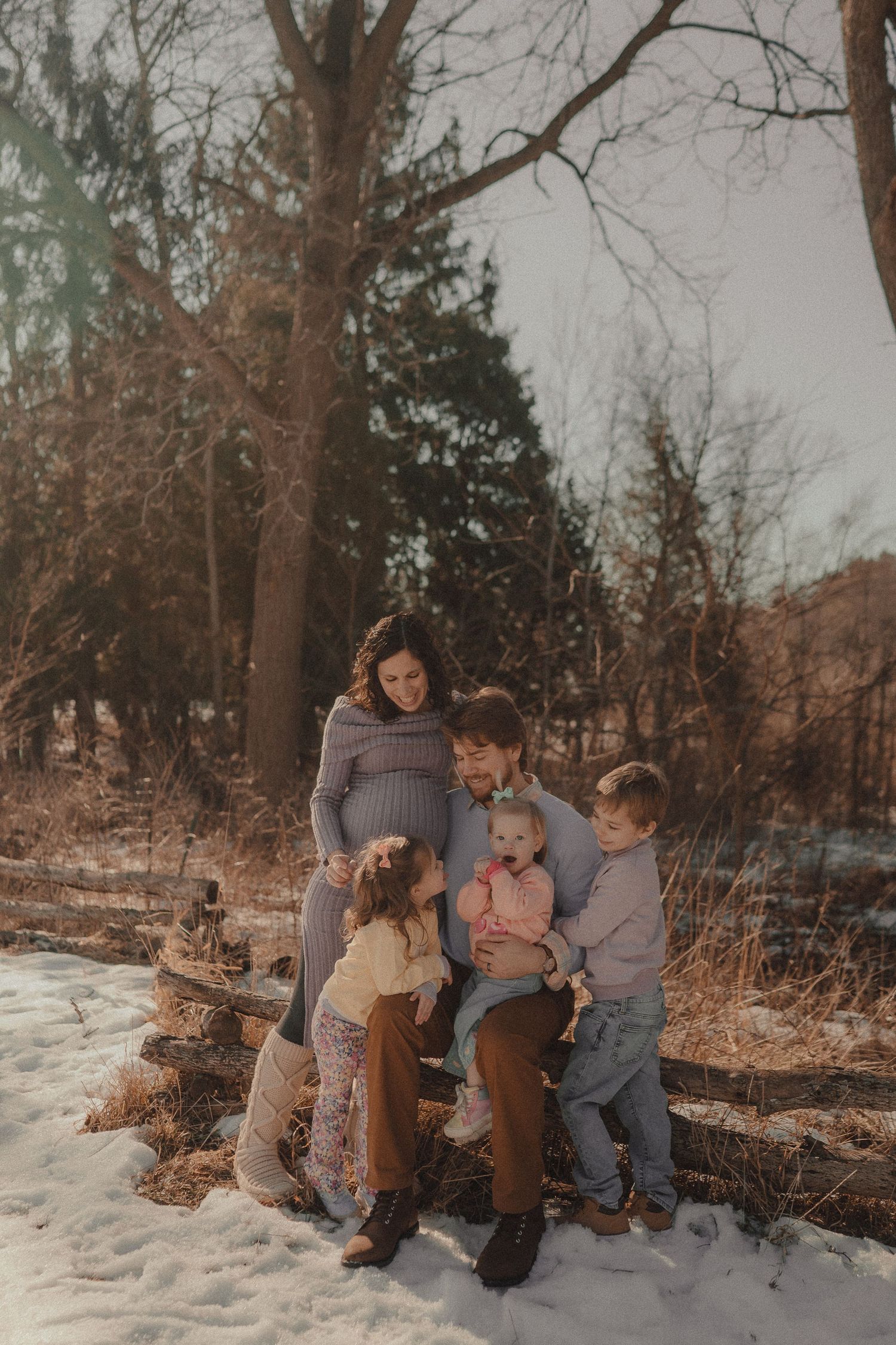 A family photo session in a winter forest setting with snow on the ground.