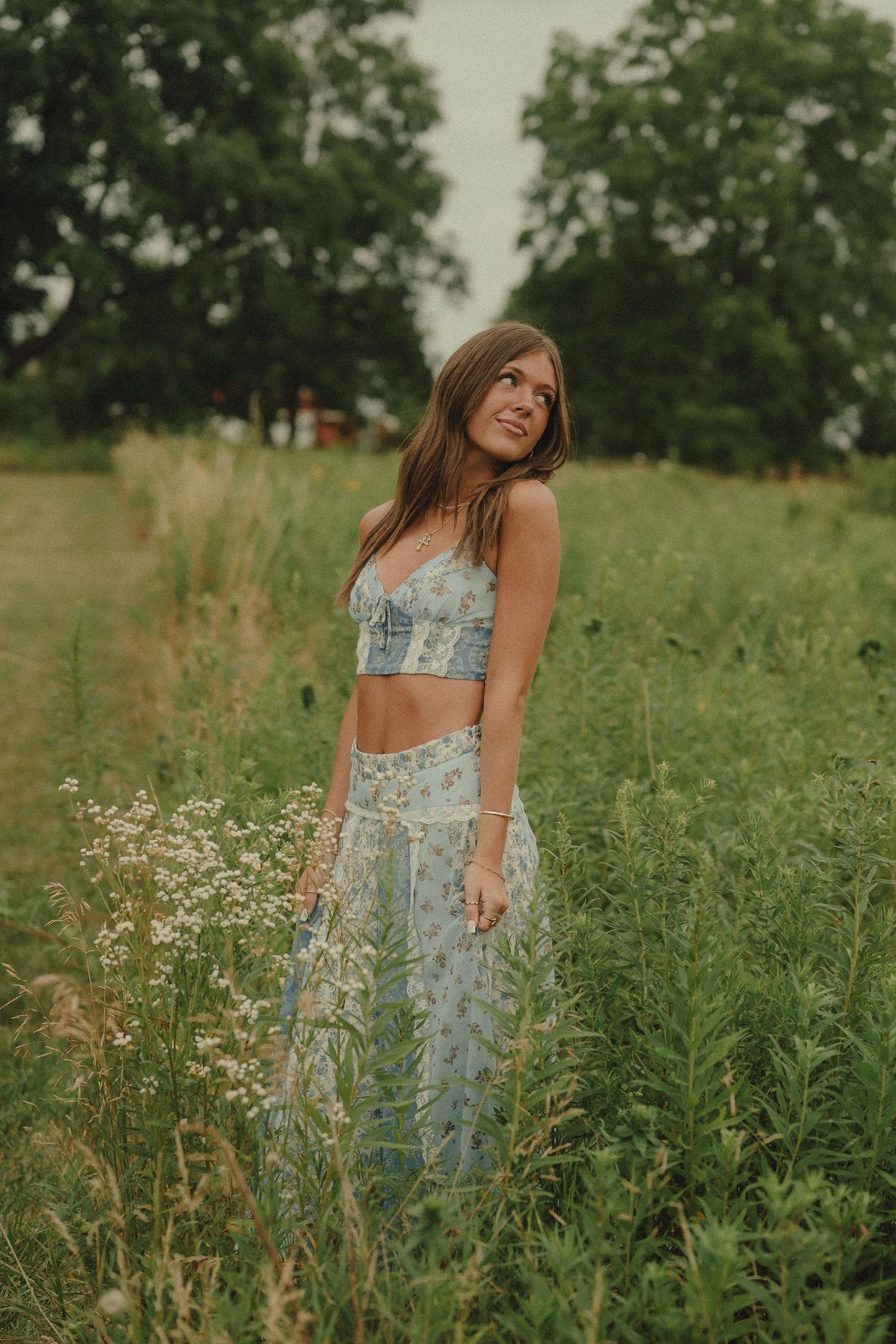 Young woman in light blue floral crop top and maxi skirt posing in a wildflower meadow.
