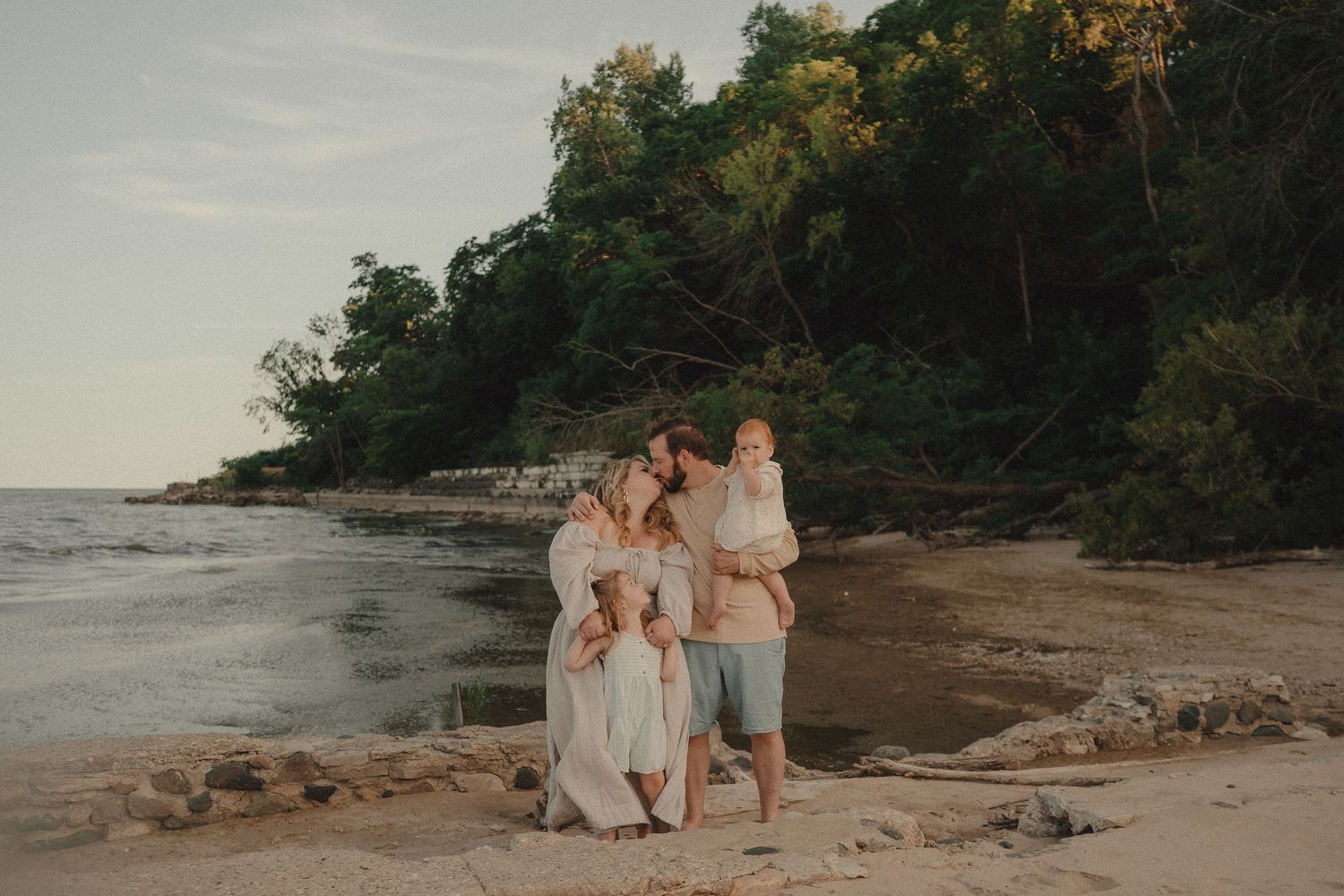 Family of four enjoying a golden hour beach moment with lush green cliffs and calm ocean waters in the background.