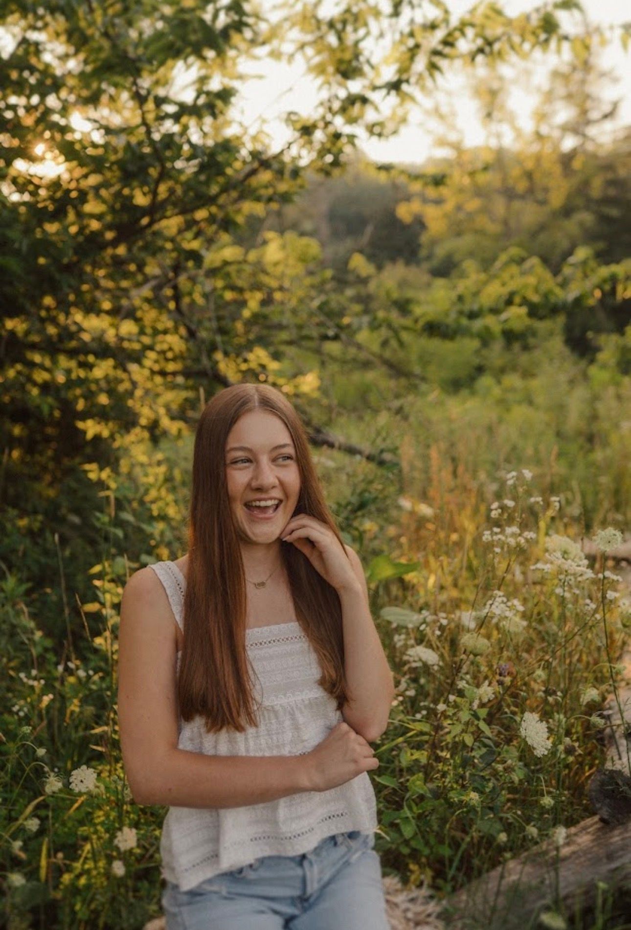 Joyful outdoor portrait amid wildflowers and greenery at golden hour.