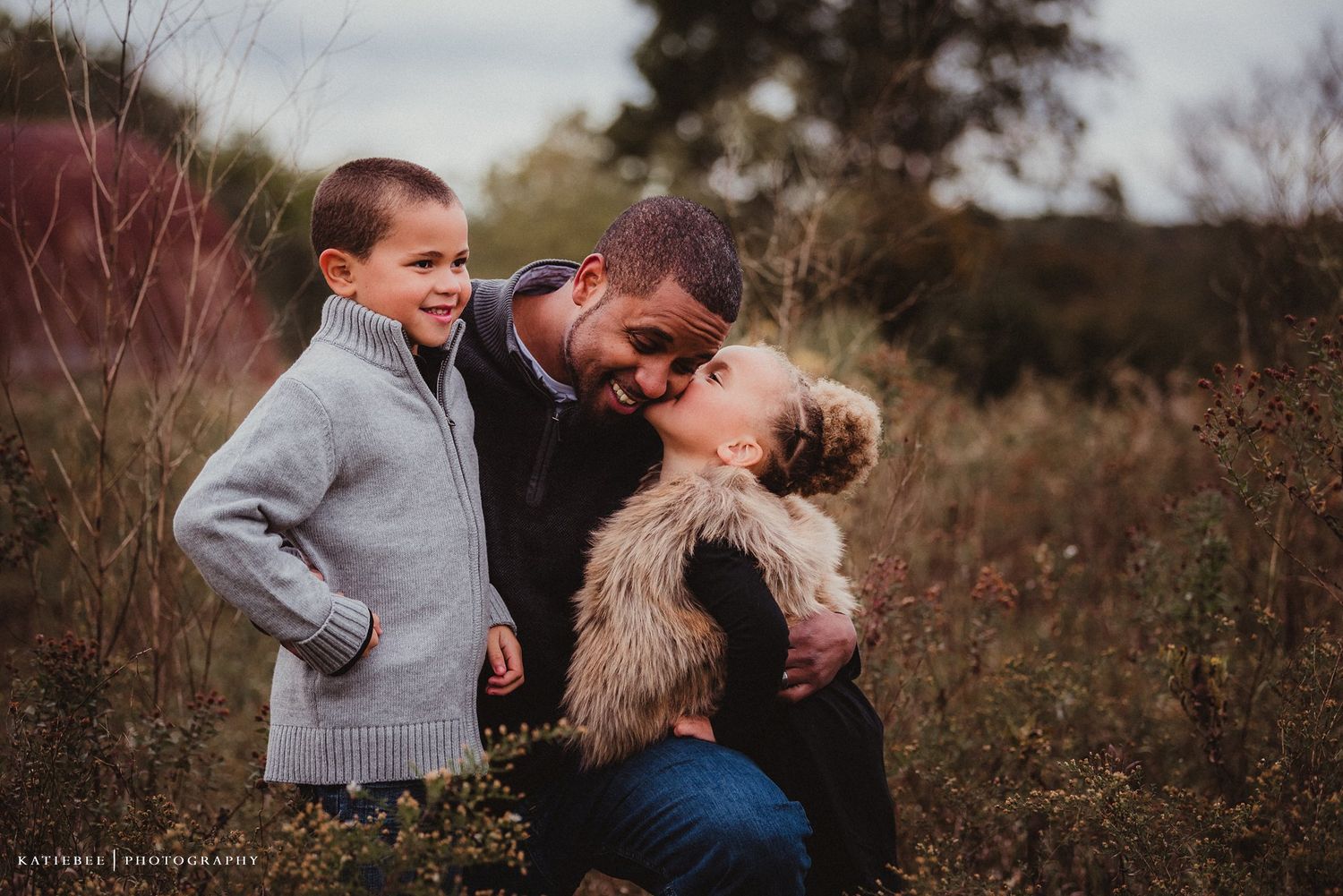Candid moment of family laughter and embraces in a field during autumn.