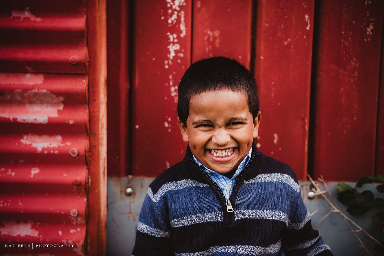 Cheerful expression captured against weathered red barn siding in casual attire.
