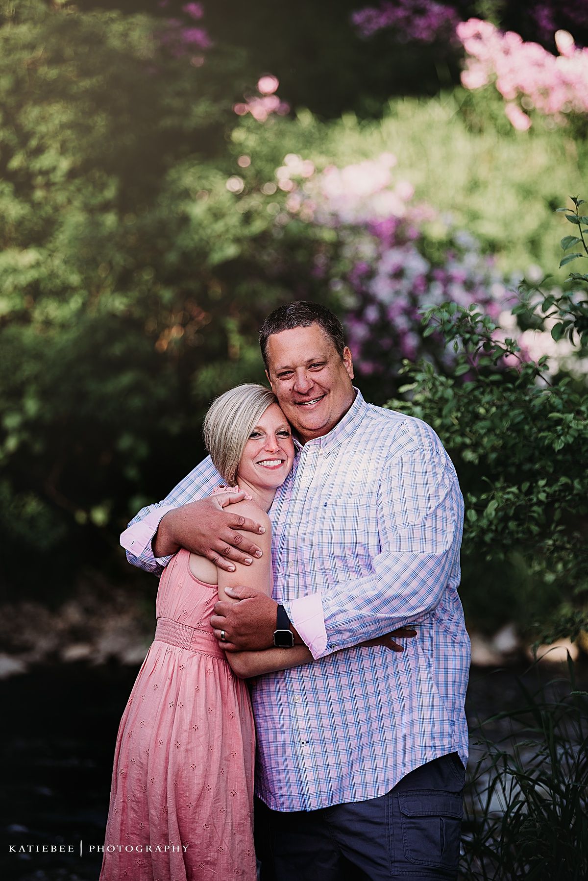 Couple embracing in pink and blue outfits against garden backdrop.