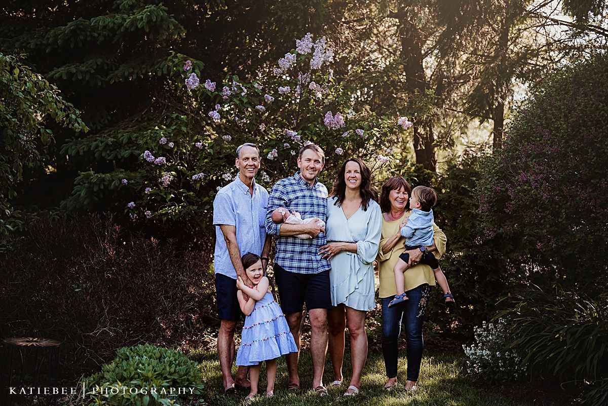 Family group poses together outdoors at sunset among trees and greenery.