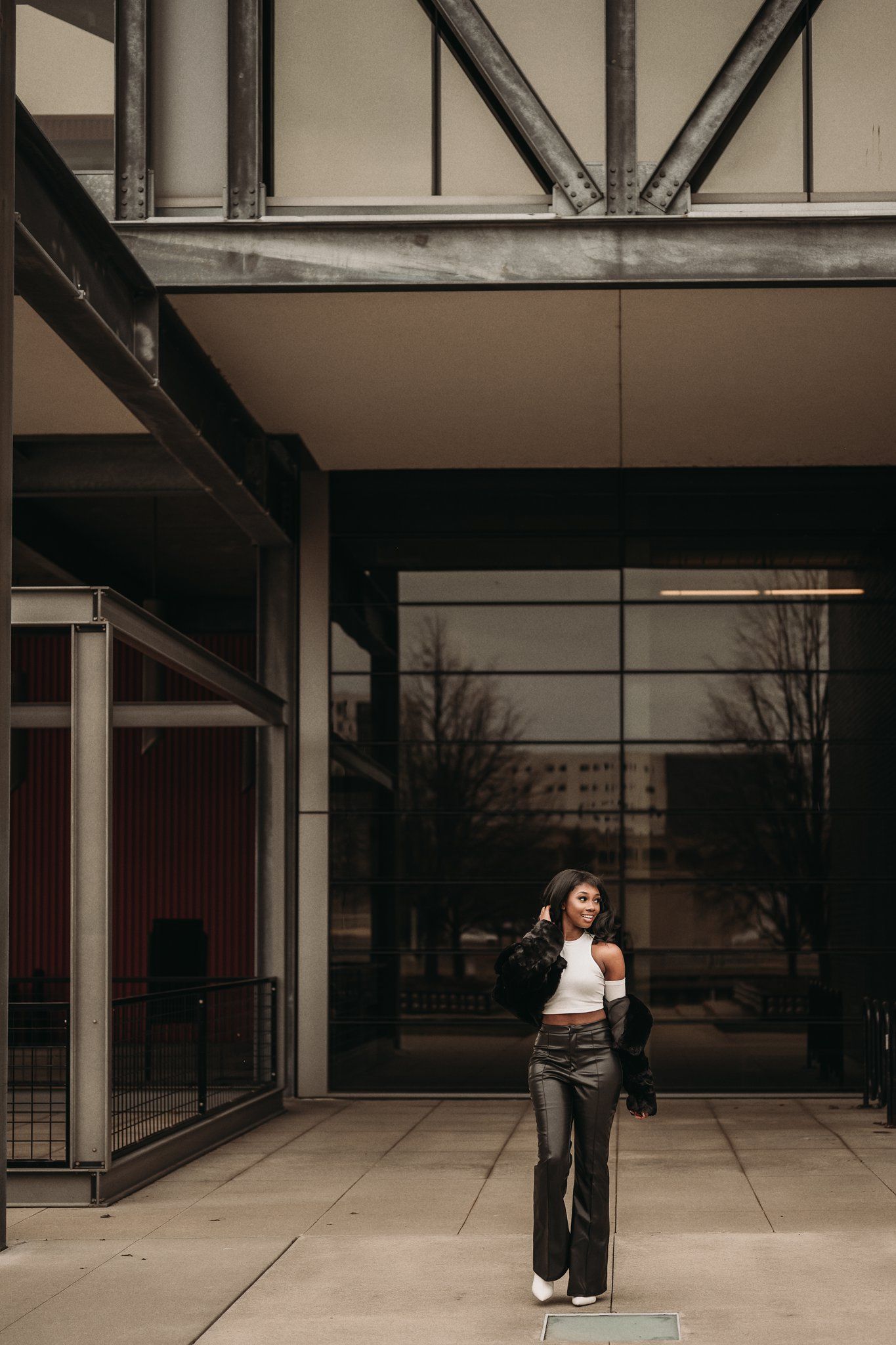 Fashion model poses confidently in front of modern industrial architecture.