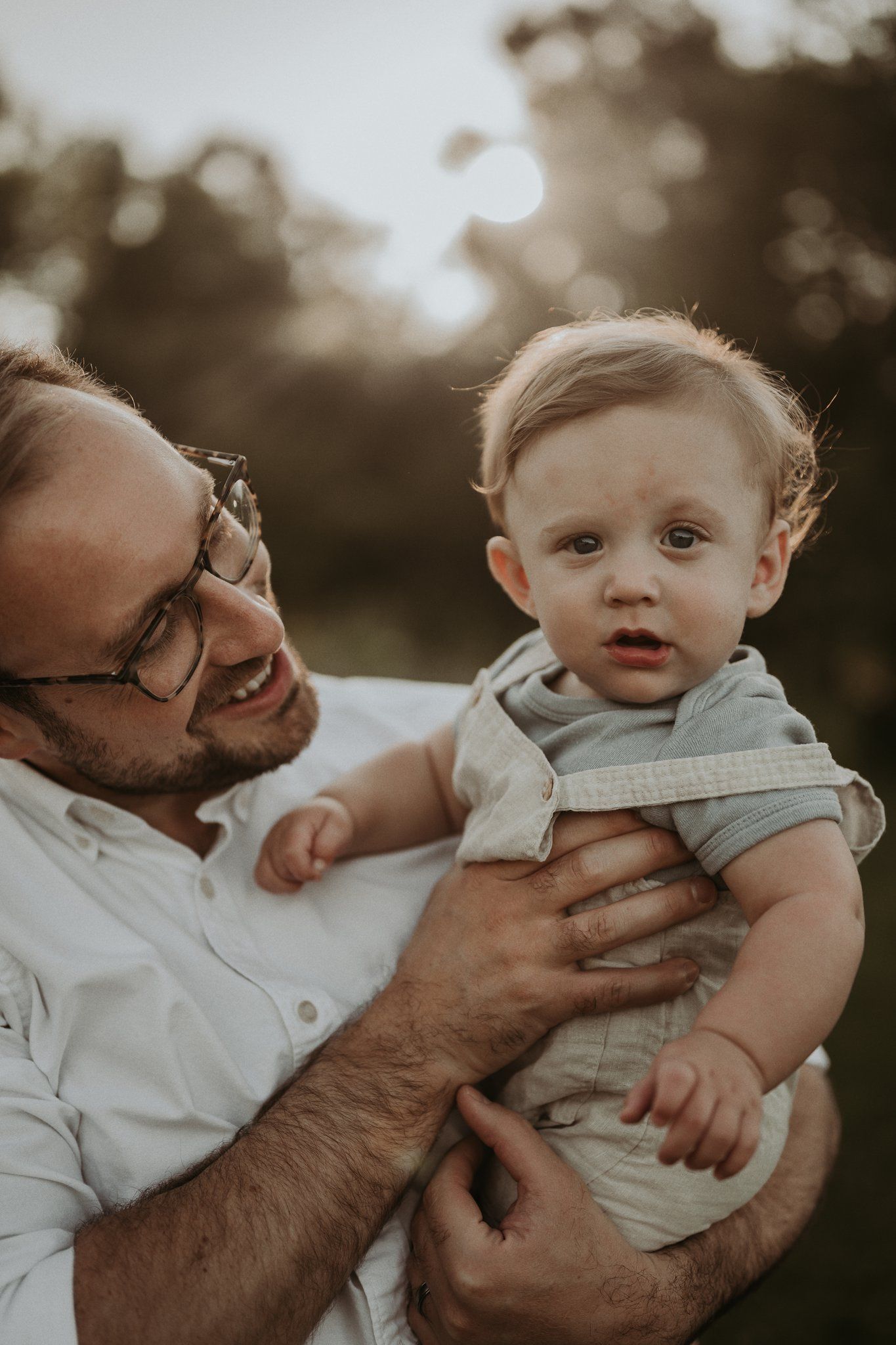 Close up portrait of baby and adult sharing a happy moment outdoors at sunset.