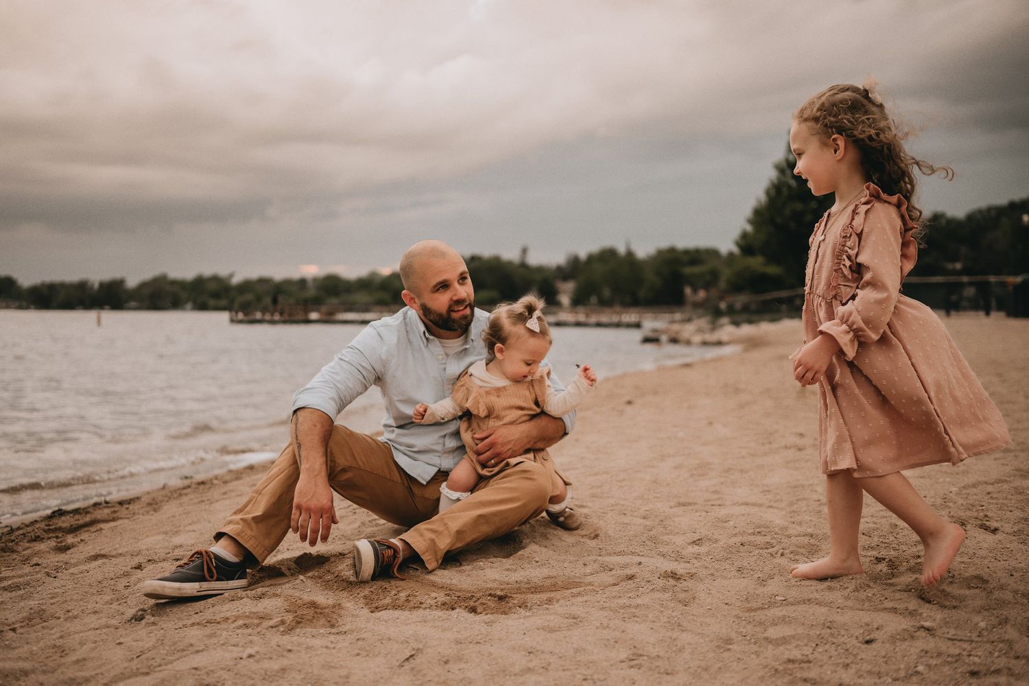 A playful family scene on a cloudy beach with boats visible in the background.