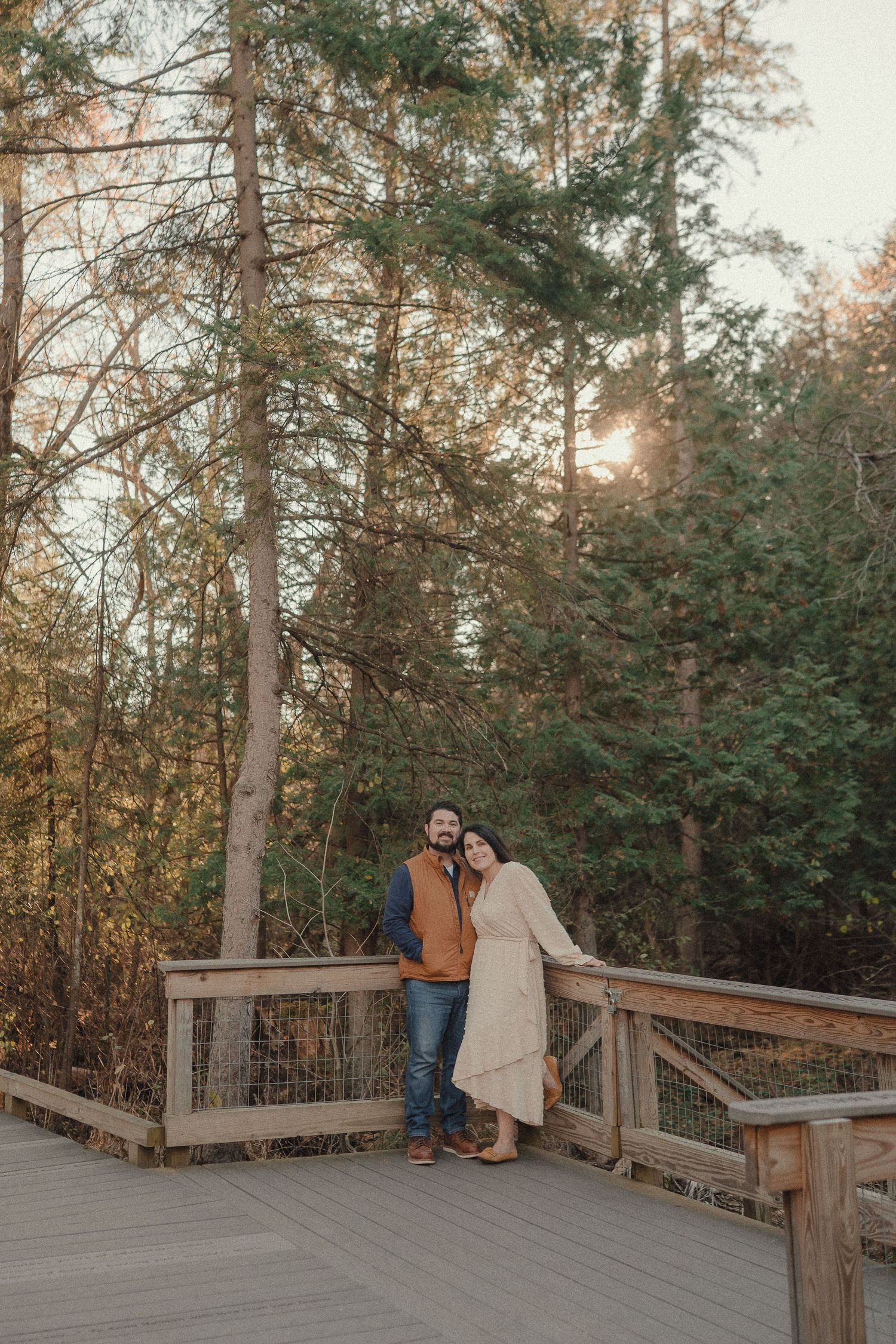 A couple enjoys tender moments on a wooden deck platform surrounded by pine trees at dusk.