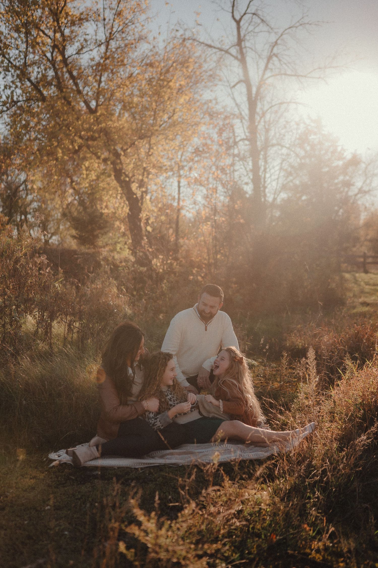 A family relaxes together on a blanket during a golden hour photoshoot in a sunlit autumn field.