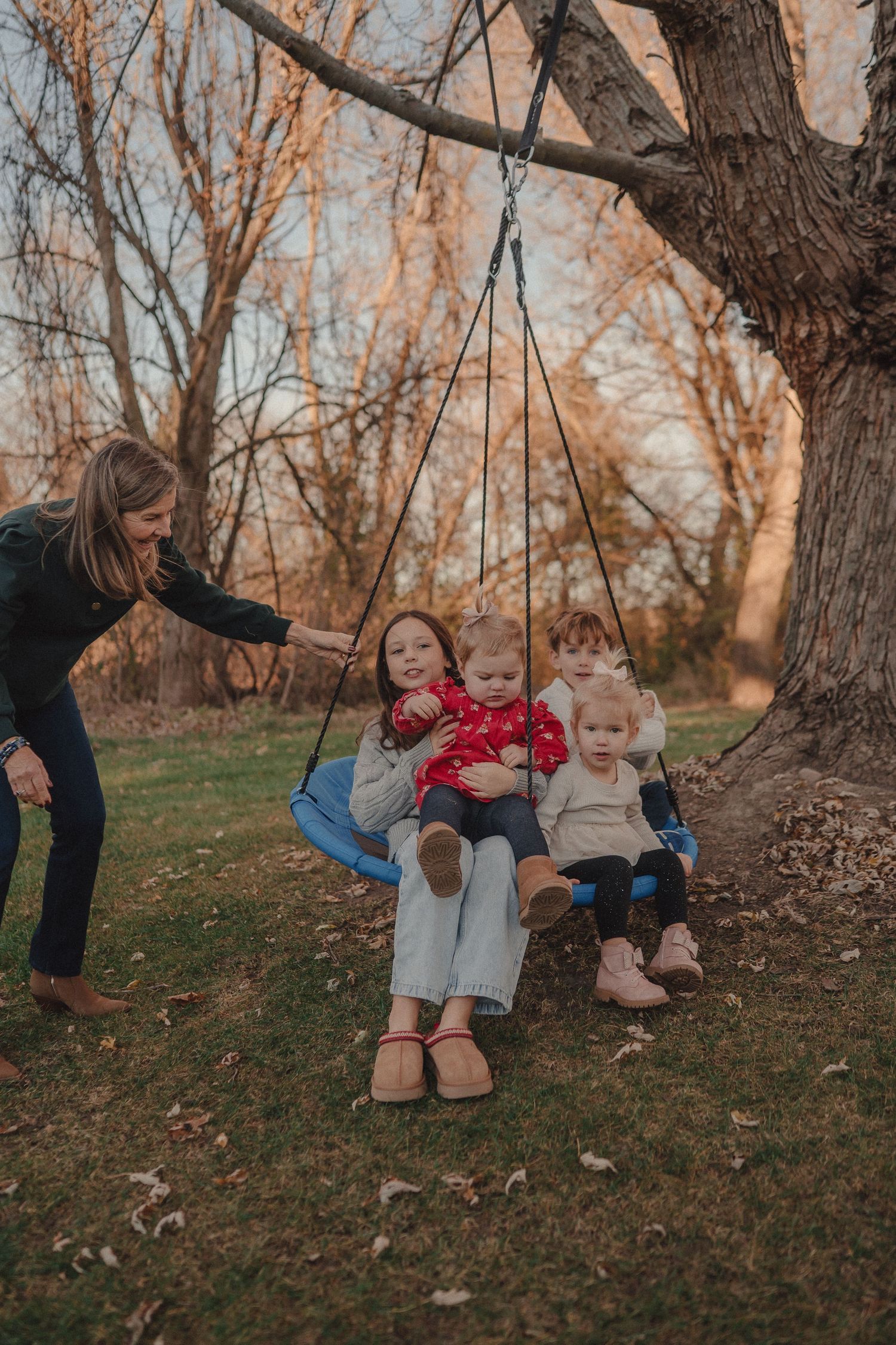 Children enjoy swinging on a tree swing while being pushed in an autumn setting with golden light filtering through.