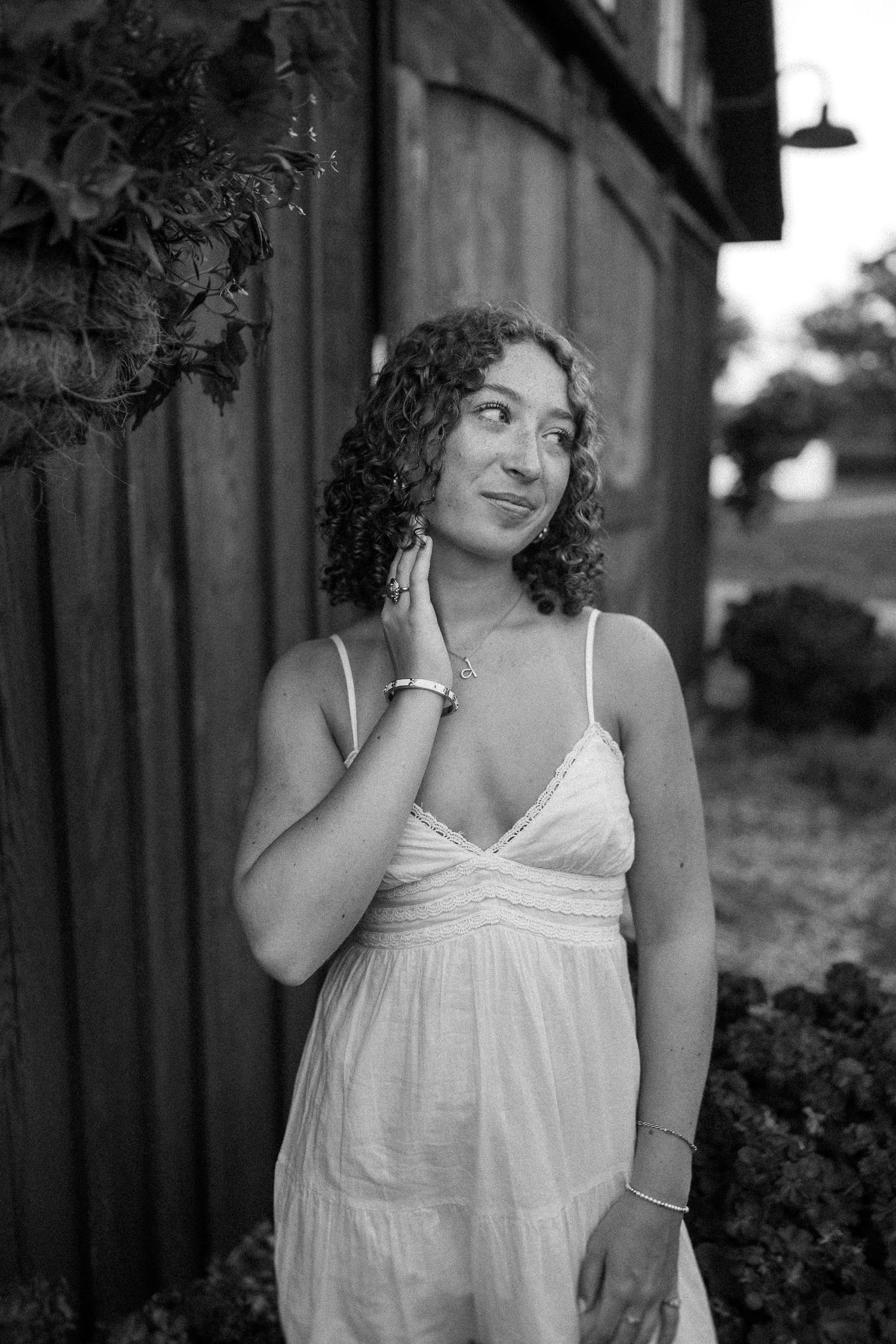 Black and white portrait of someone in a flowing white sundress standing against a building exterior.