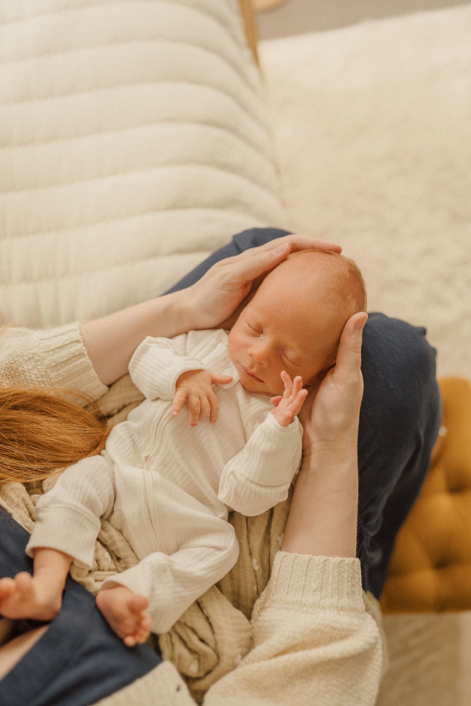 Baby in white clothing being cradled in loving hands while resting on navy blue fabric.