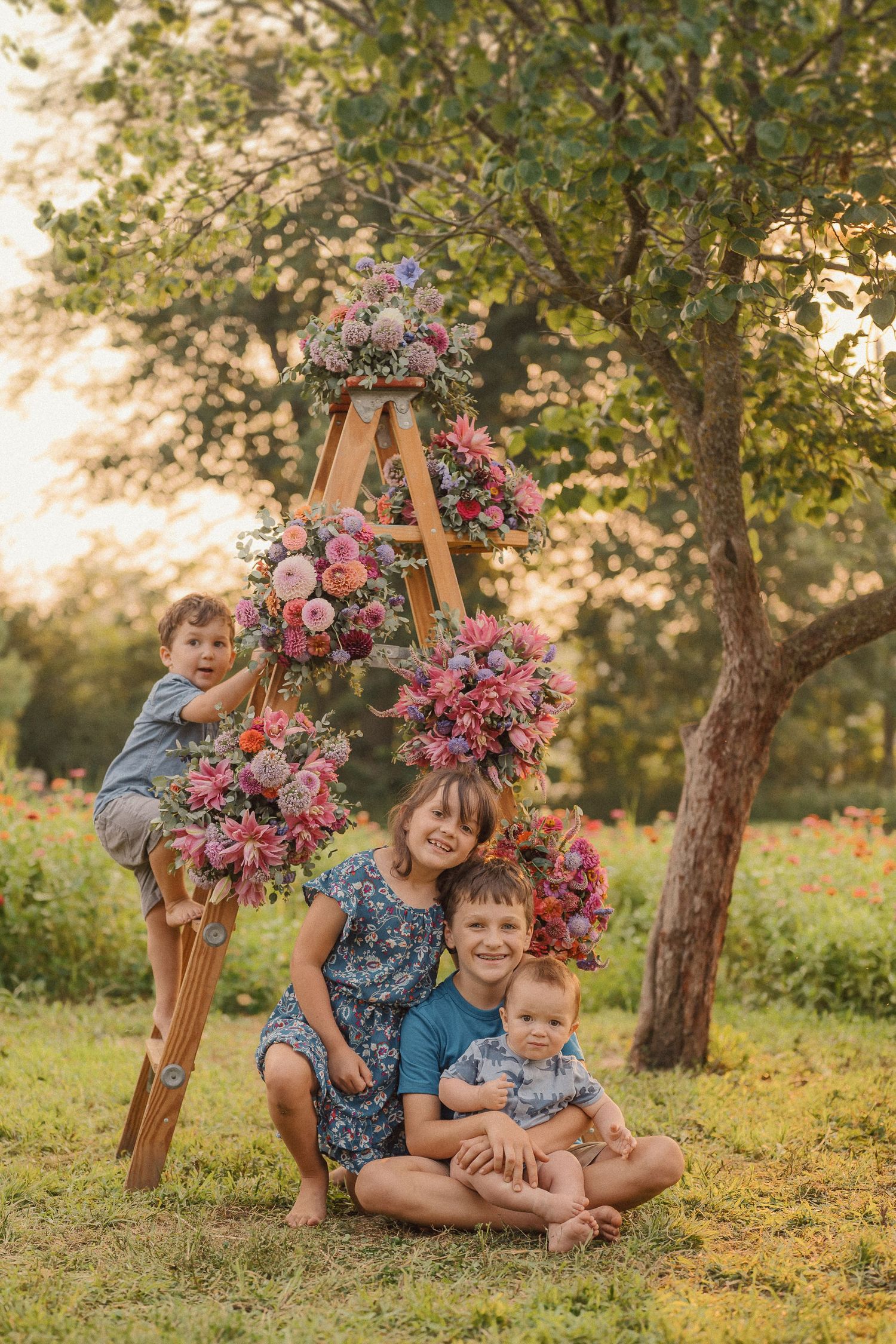 A sunny outdoor photoshoot with a wooden ladder decorated with vibrant pink and purple floral arrangements.