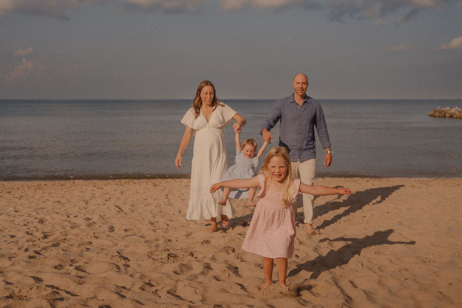 A family walks together along a scenic beach at sunset with the ocean in the background.