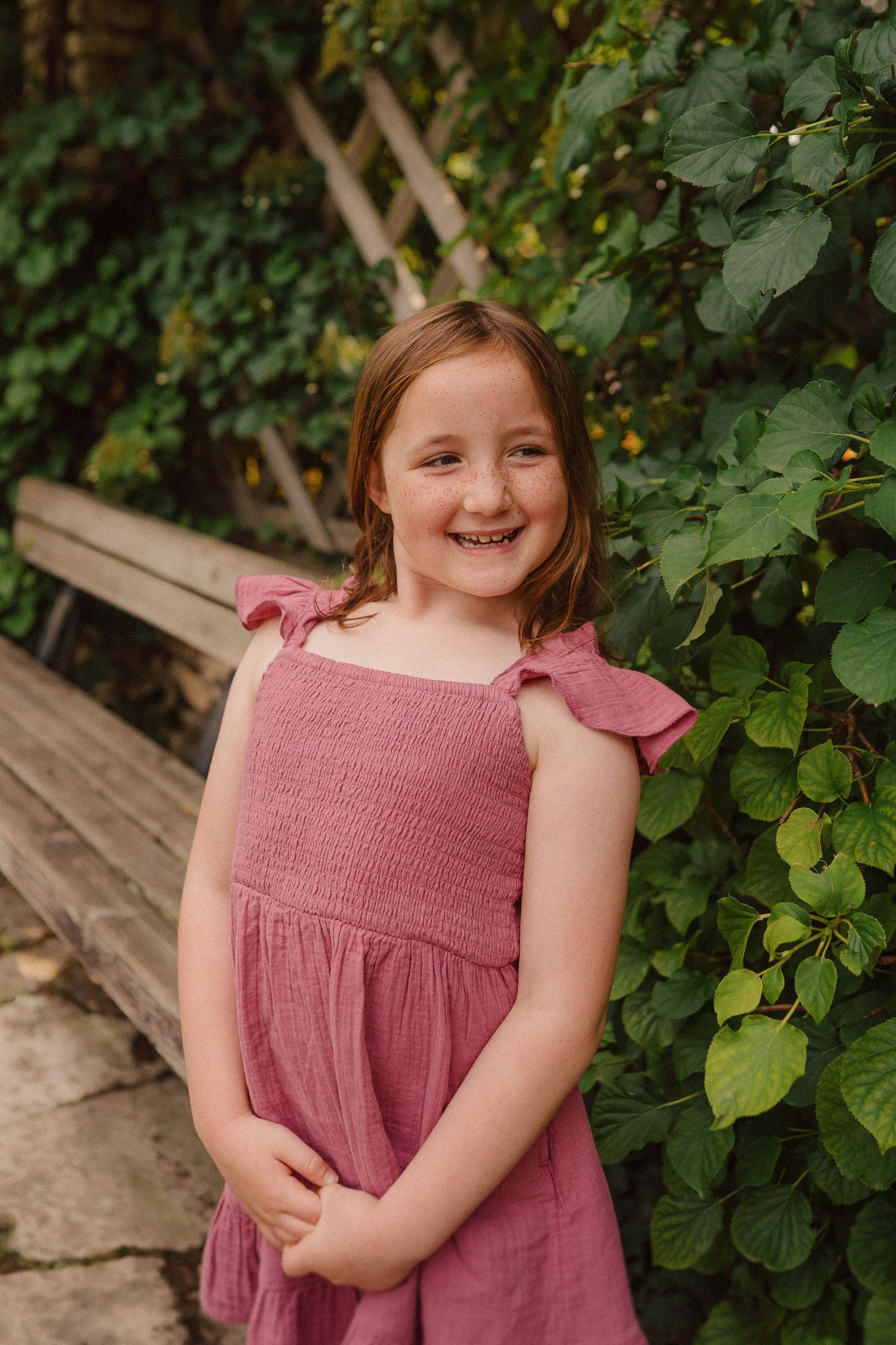 A summer garden portrait featuring a pink smocked dress against lush green foliage.