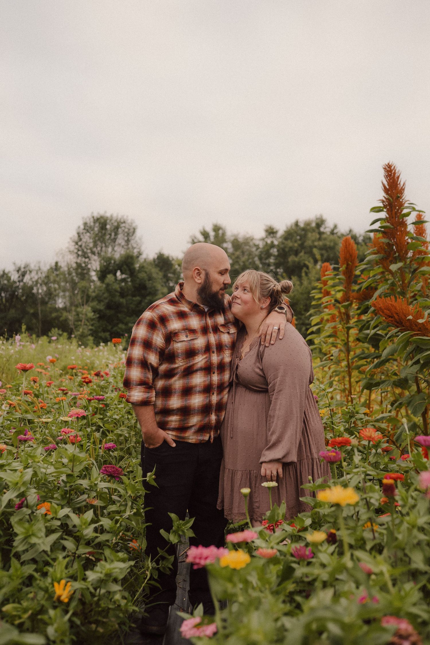 A couple embraces lovingly in a blooming wildflower field filled with colorful zinnias and sunflowers on an autumn day.