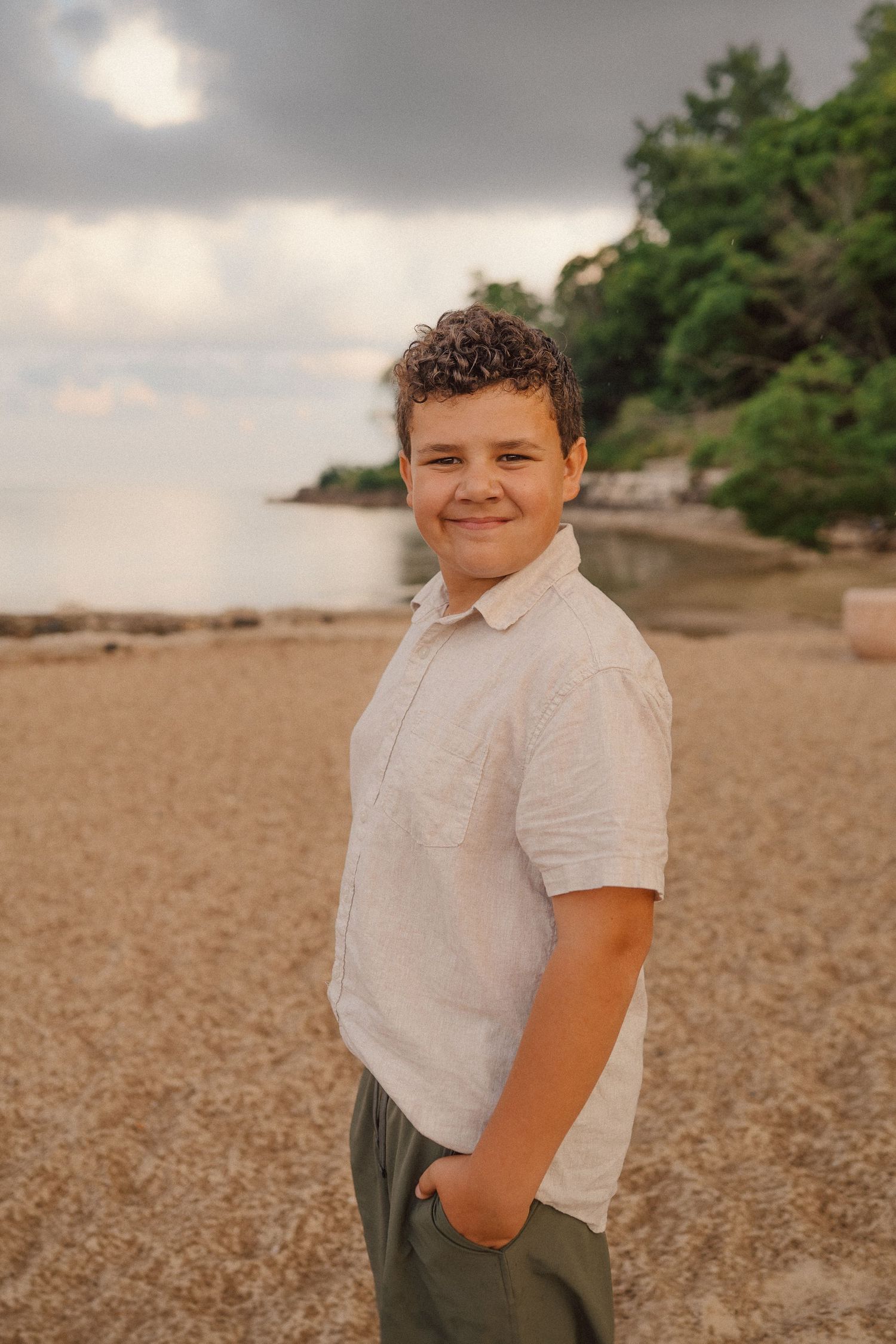 A beachside portrait shows someone smiling on a sandy shore with moody skies overhead.