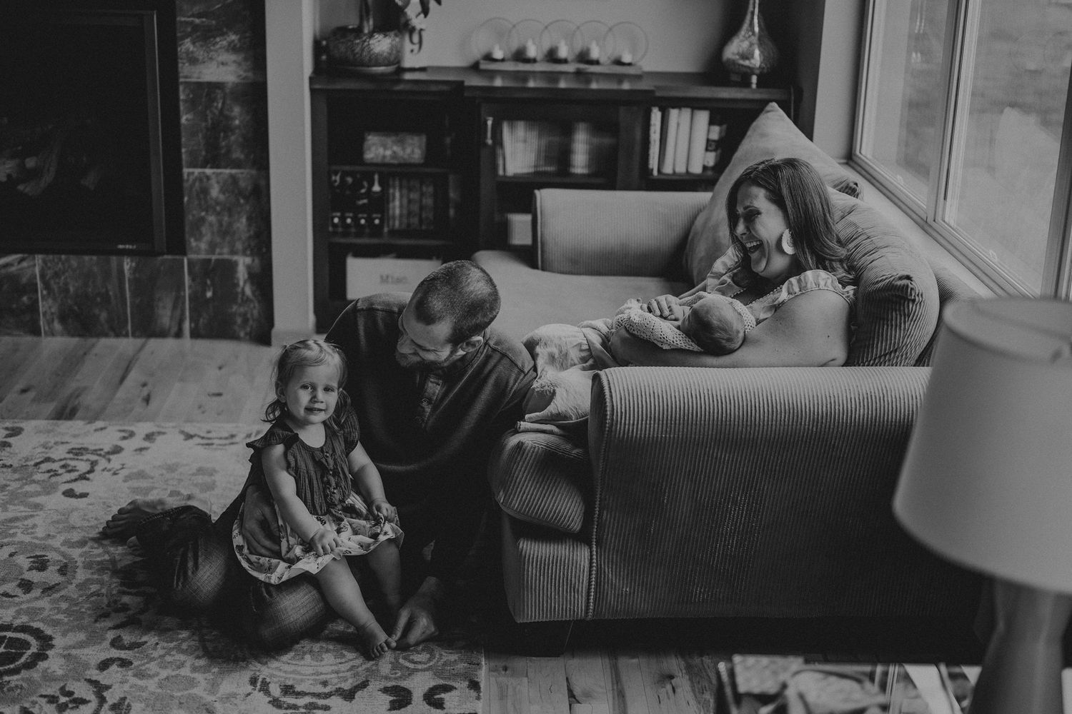 A cozy living room scene with family members relaxing together on and around a brown sofa near a window.