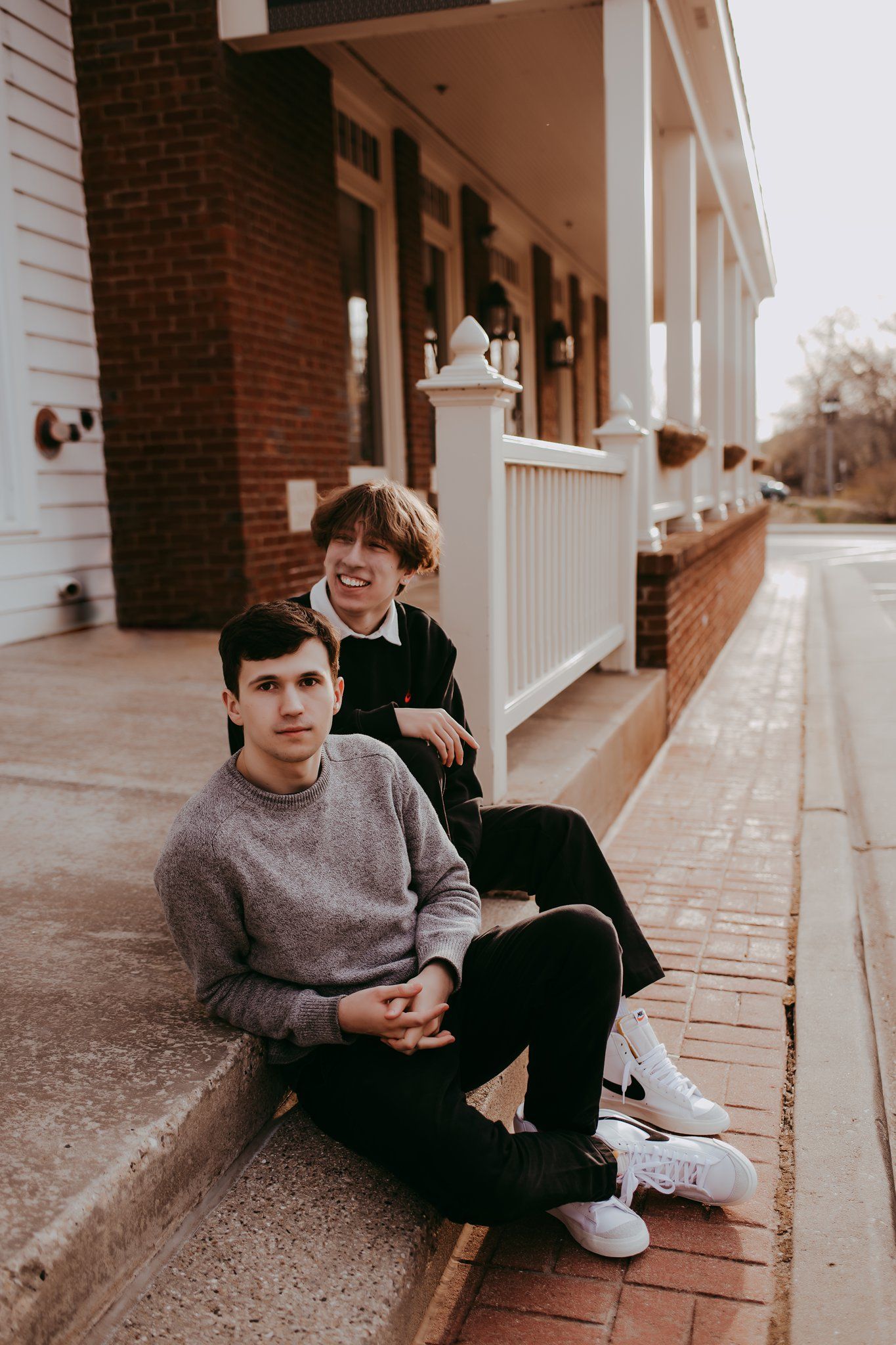 Two people sitting on concrete steps share a relaxed moment outside a building.