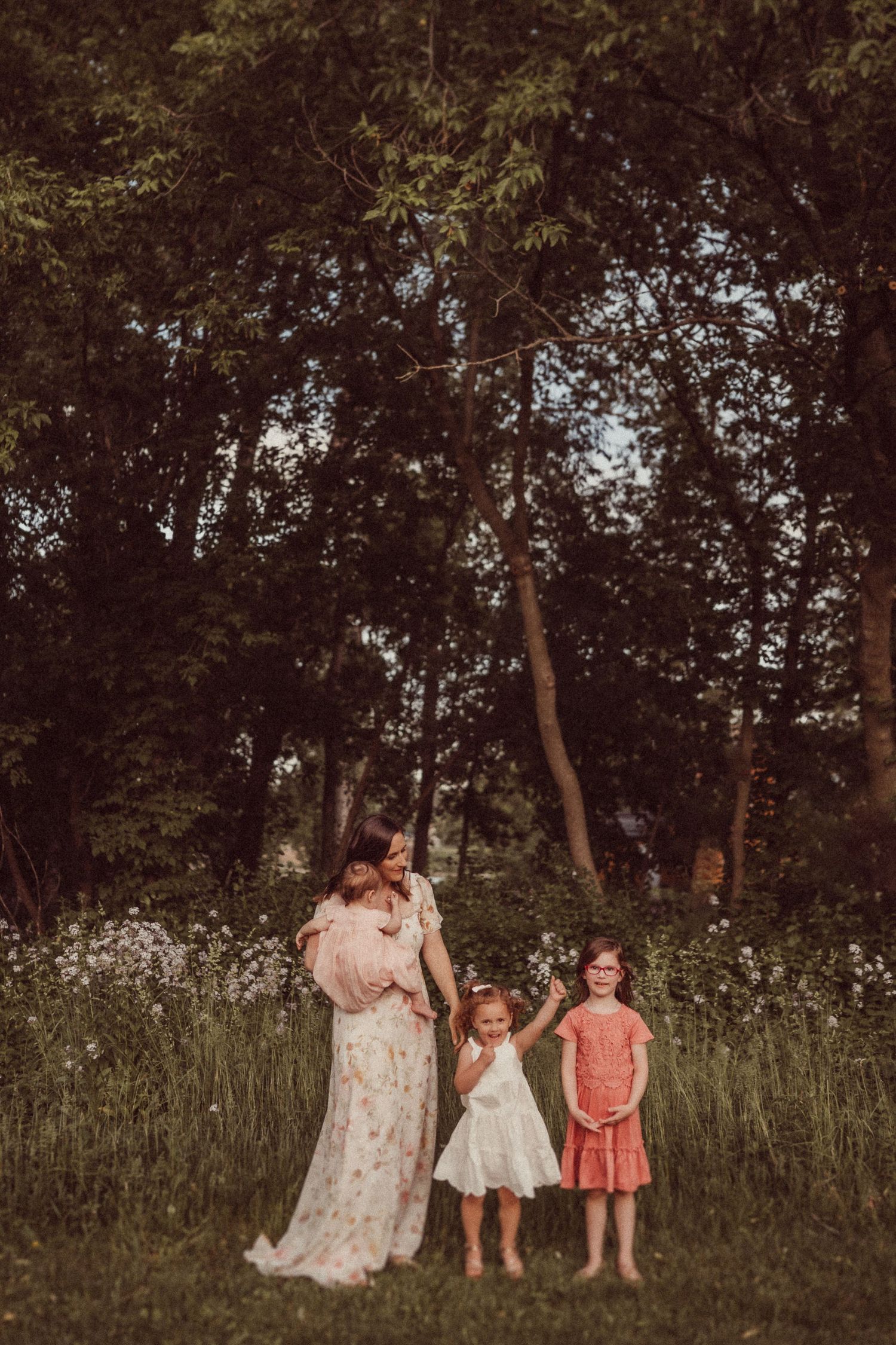 A family portrait in a wildflower meadow with tall trees creating a natural backdrop.
