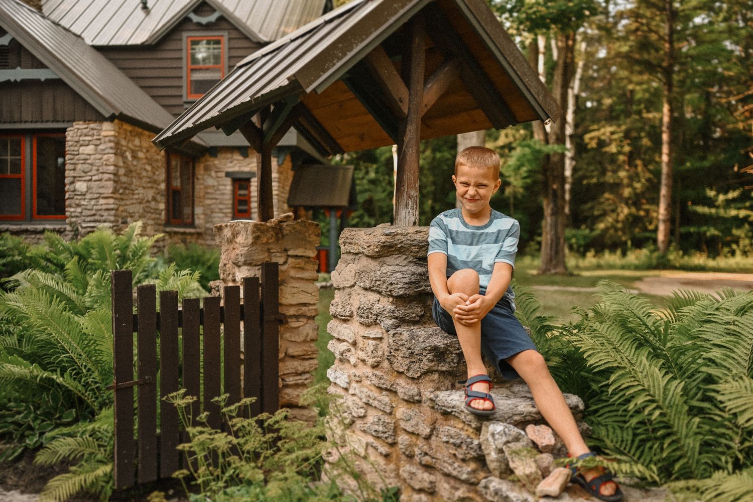 A rustic stone and wood cottage with ferns growing along a stone wall entrance.