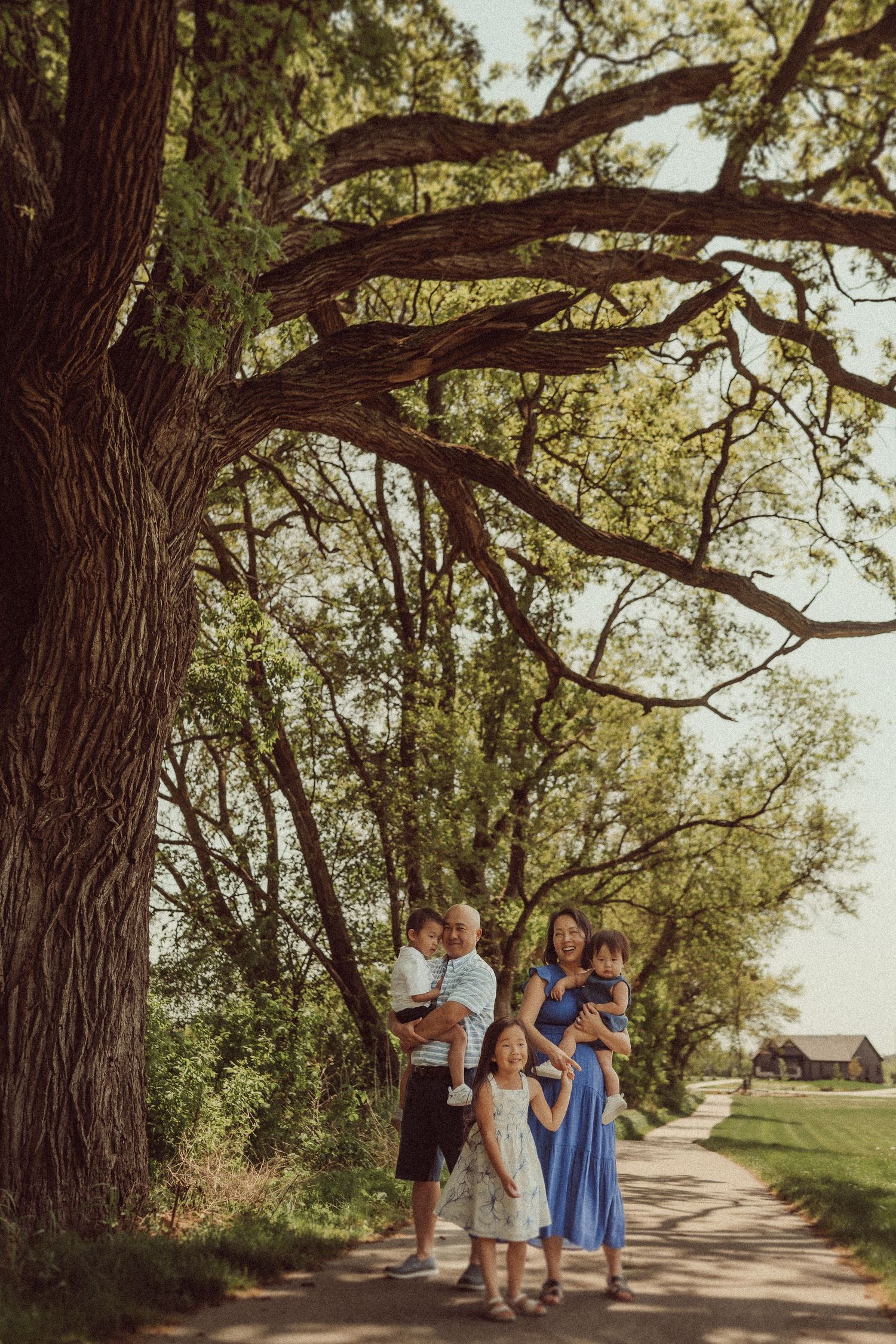 Family portrait beneath a grand old tree with sprawling branches on a dirt path.