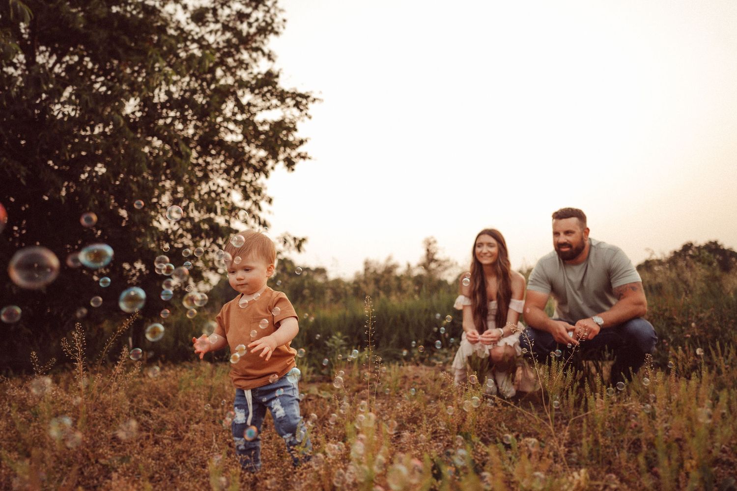 A playful outdoor family scene at sunset with soap bubbles floating through a golden field.