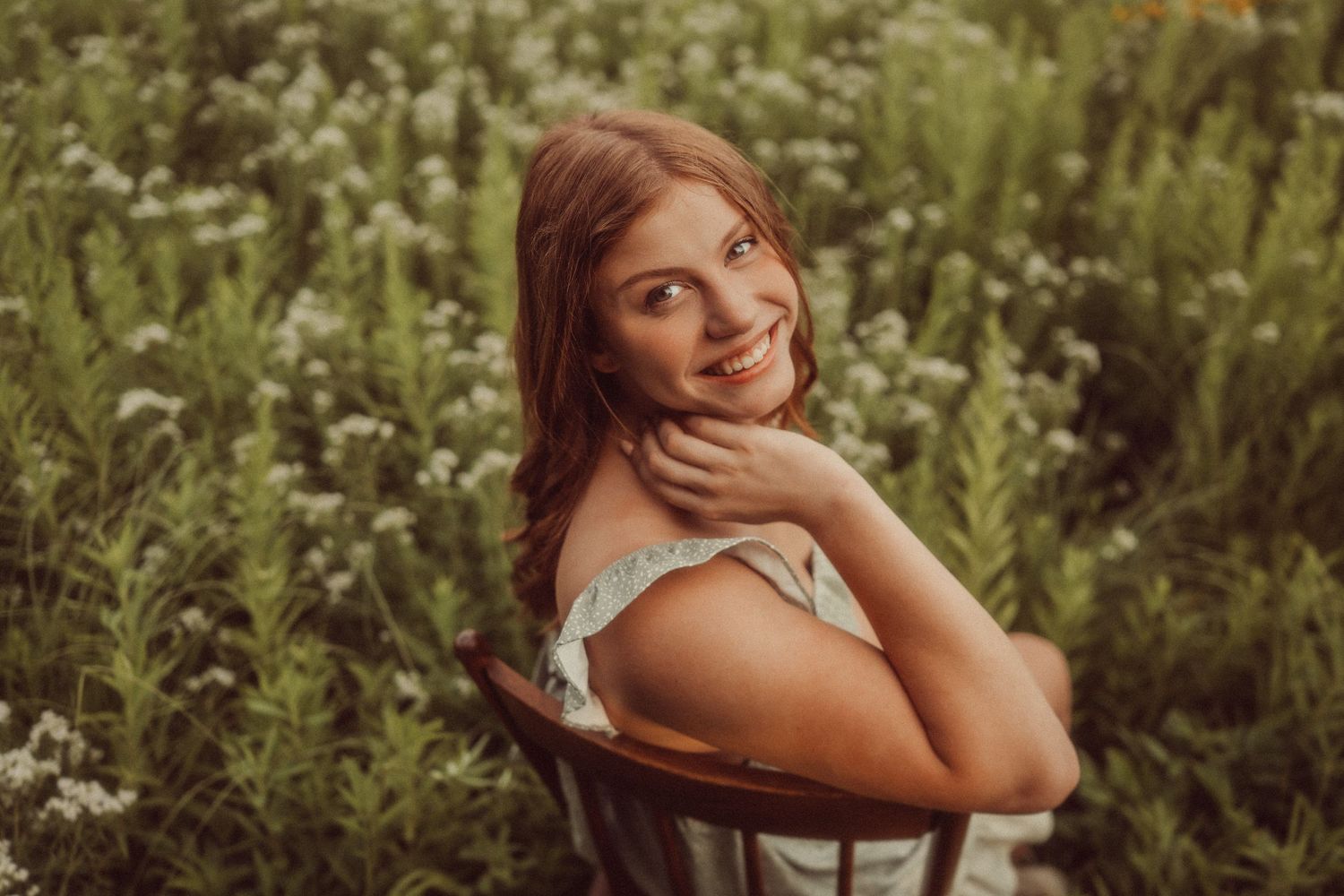 Person poses playfully in chair surrounded by tall wildflowers and natural meadow grasses.