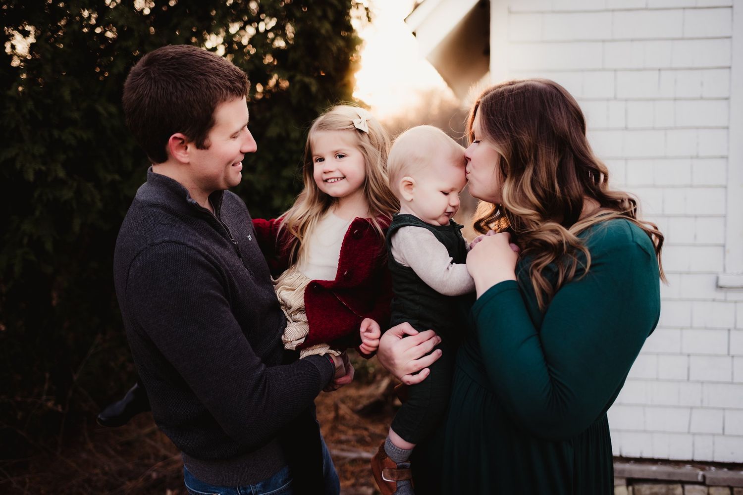 Intimate family moment captured during sunset against white brick building.