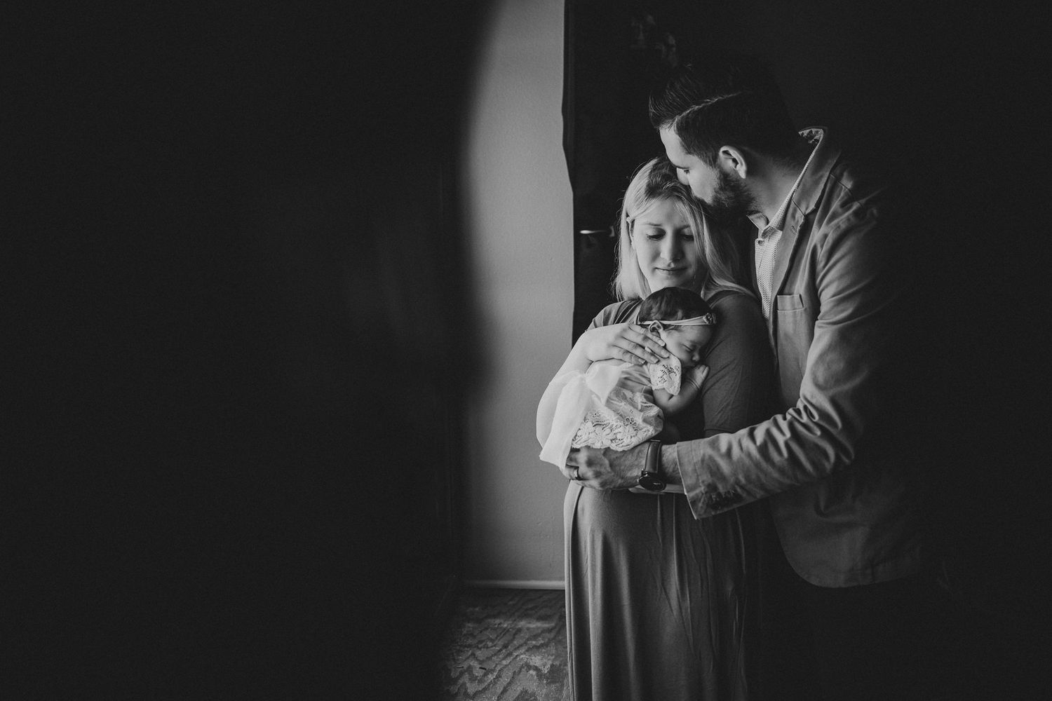 Black and white portrait of family embracing while holding their newborn baby.