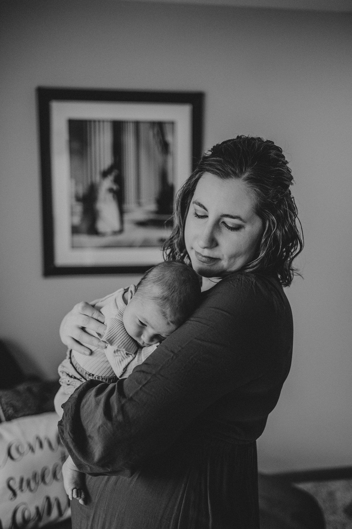 A moody black and white portrait of a parent cradling their sleeping newborn baby.