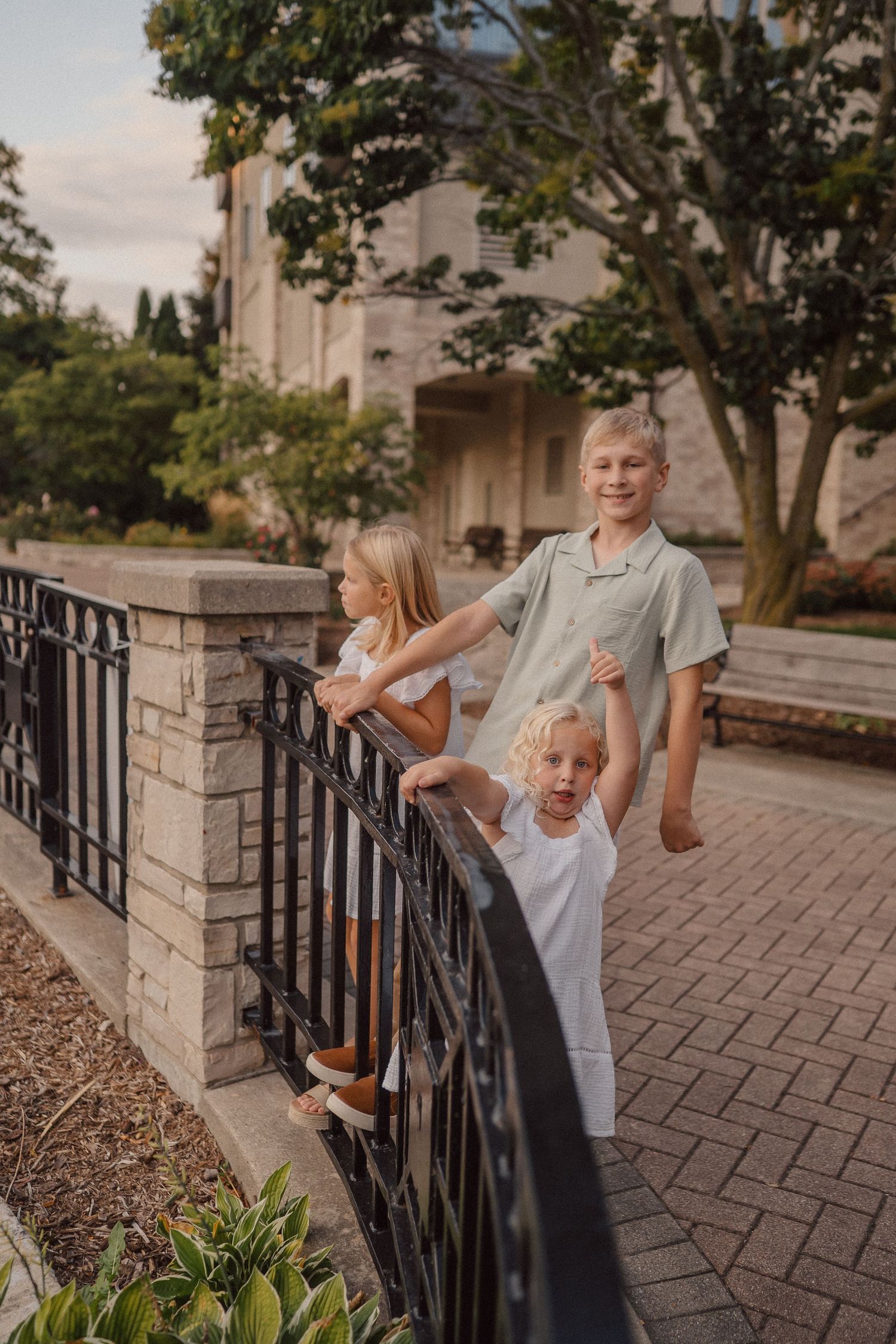 Children playing and posing near a decorative iron railing with trees and buildings in the background.